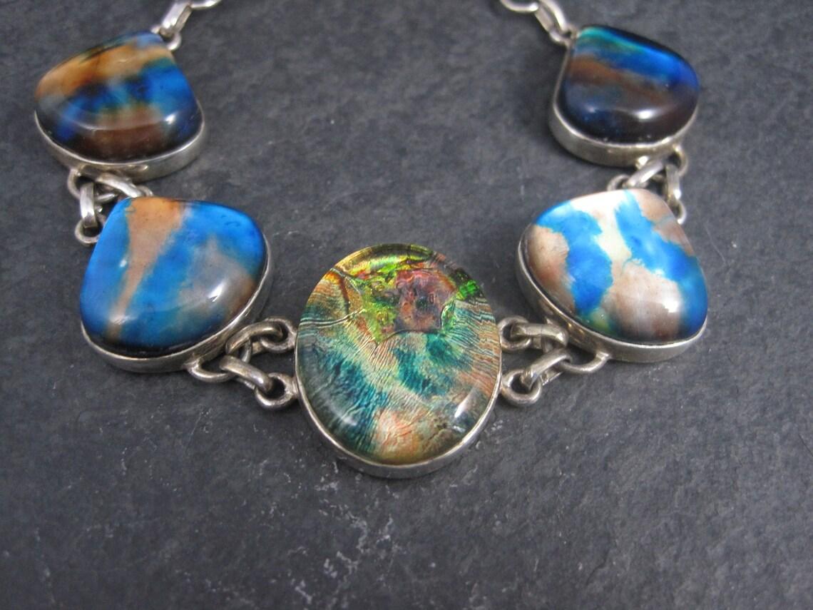 This gorgeous bracelet is sterling silver with dichroic glass stones.

Measurements: 15/16 of an inch at its widest
Adjustable from 6 3/4 to 8 inches

Weight: 30.2 grams

Condition: Excellent