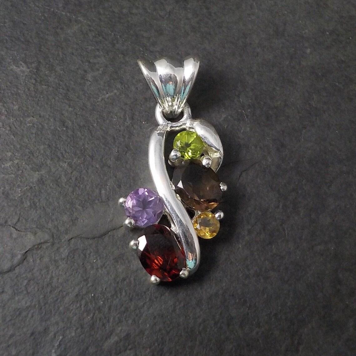 Ce magnifique pendentif est en argent sterling.
Il contient des pierres précieuses telles que le péridot, le quartz fumé, la citrine, l'améthyste et le grenat.

Dimensions : 11/16 par 1 1/2 pouces
La caille peut accueillir une chaîne jusqu'à 5
