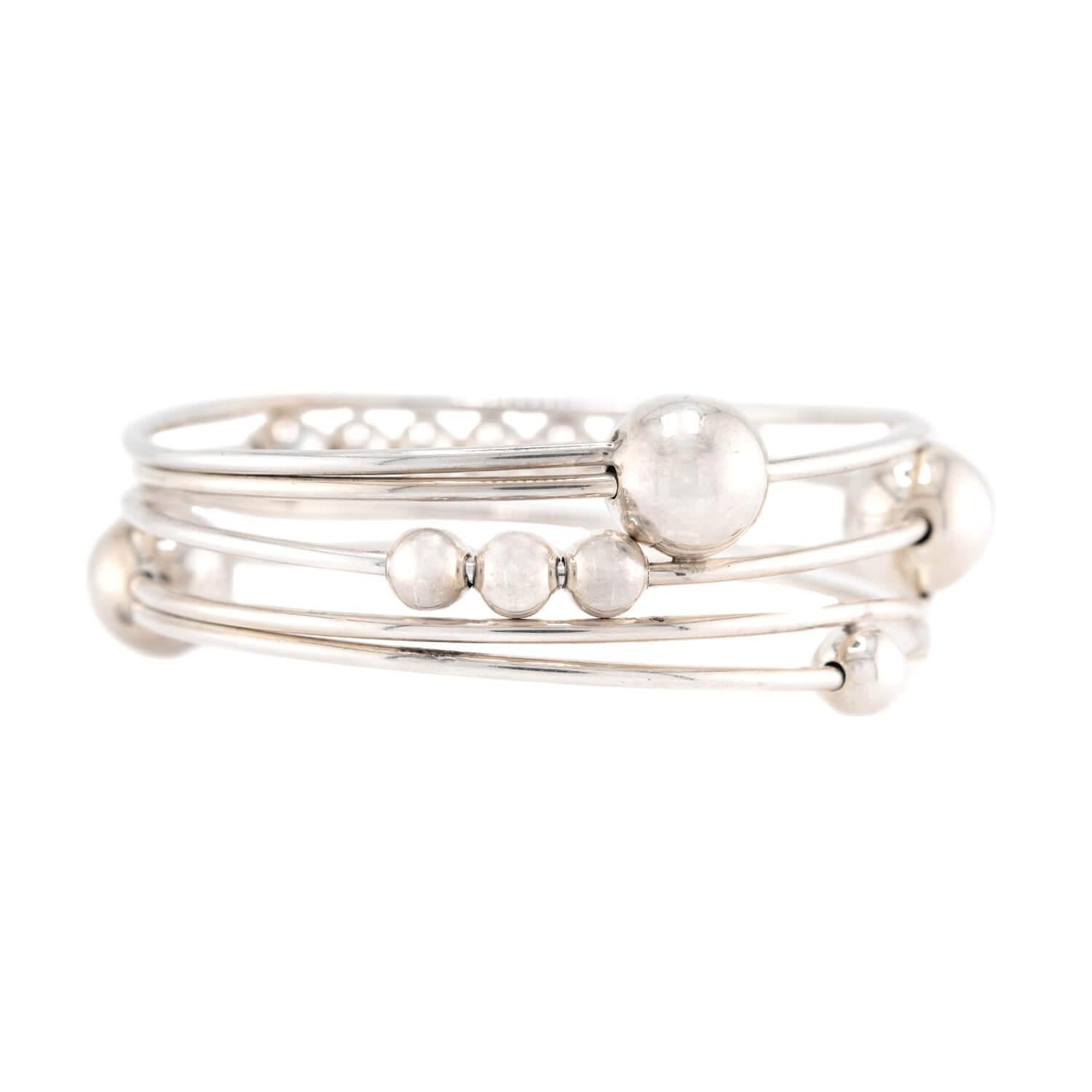 A beautiful geometric bangle bracelet from the Vintage (ca1960s) era! Crafted in sterling silver, this piece is comprised of five thin interlocking bangle bracelets. Thirteen three-dimensional balls are dispersed amongst the bangle, which graduate