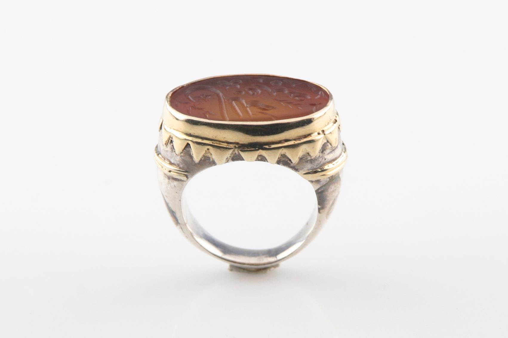 The silver ring features a golden color glass intaglio set within a gold plated bezel, and gold plated banded shoulders, completed by a five millimeter wide band.
Size: 10
Band Width: 5 mm
Face Size: 1 x 5/8 inches
Metal: 925 Sterling Silver
Weight: