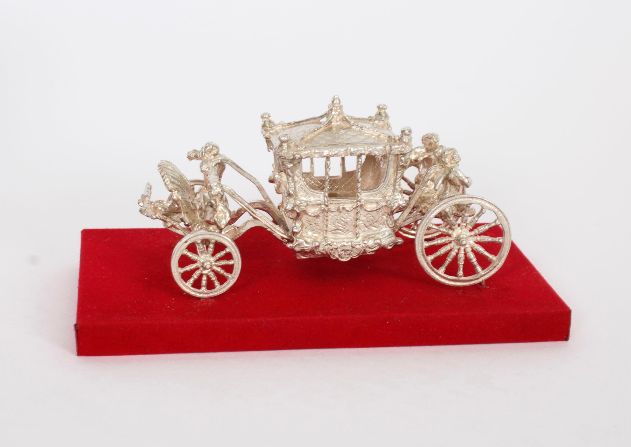 Un attraente modello in argento della carrozza dell'incoronazione della Regina, con marchio di Birmingham 1977 e marchio di fabbrica di Toye, Kenning & Spencer Ltd su una base di velluto rosso.

Gold State Coach, un'elegante carrozza chiusa che