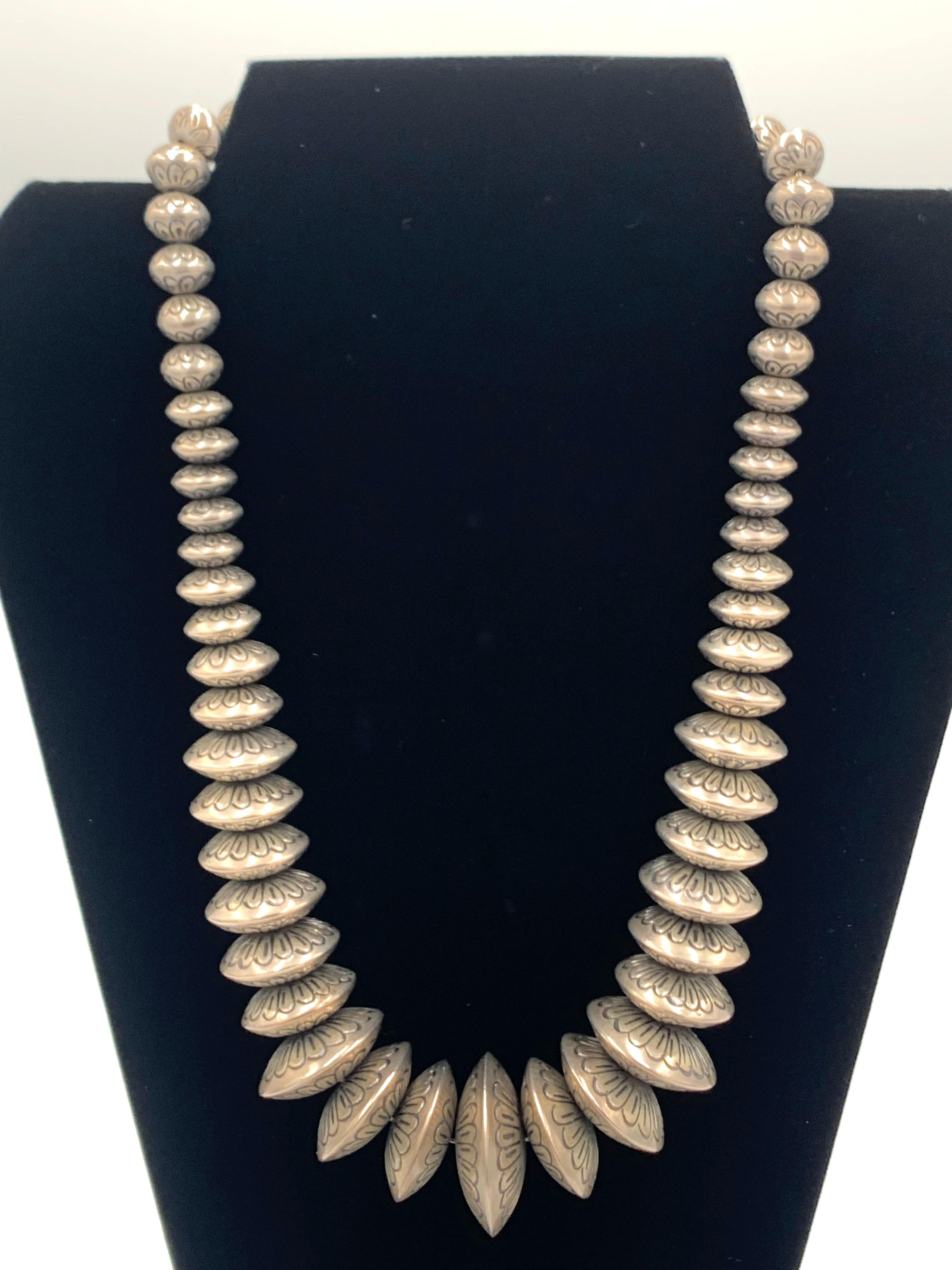 Questa collana in argento sterling a filo unico presenta 57 perle Navajo lavorate a mano di dimensioni graduali, rifinite con una patina naturale che ne esalta il carattere vintage. La perla centrale più grande misura 1,5 cm di diametro e si