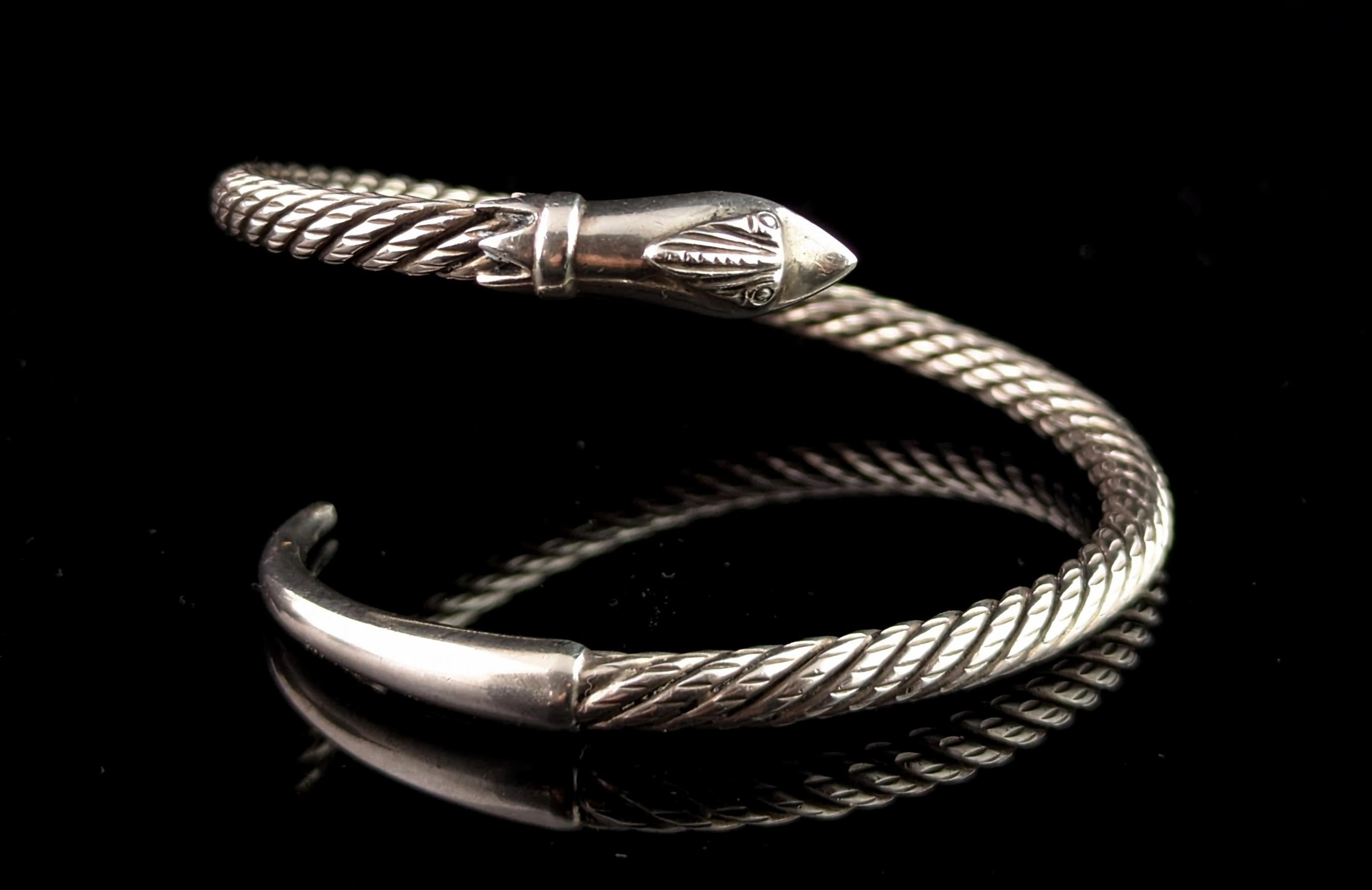 A superbly stylish vintage sterling silver snake bangle.

It is a cross over or bypass style open bangle with a snake head as one finial and the tail as the other, the body of the bangle is made up of a rope twist style good quality sterling silver