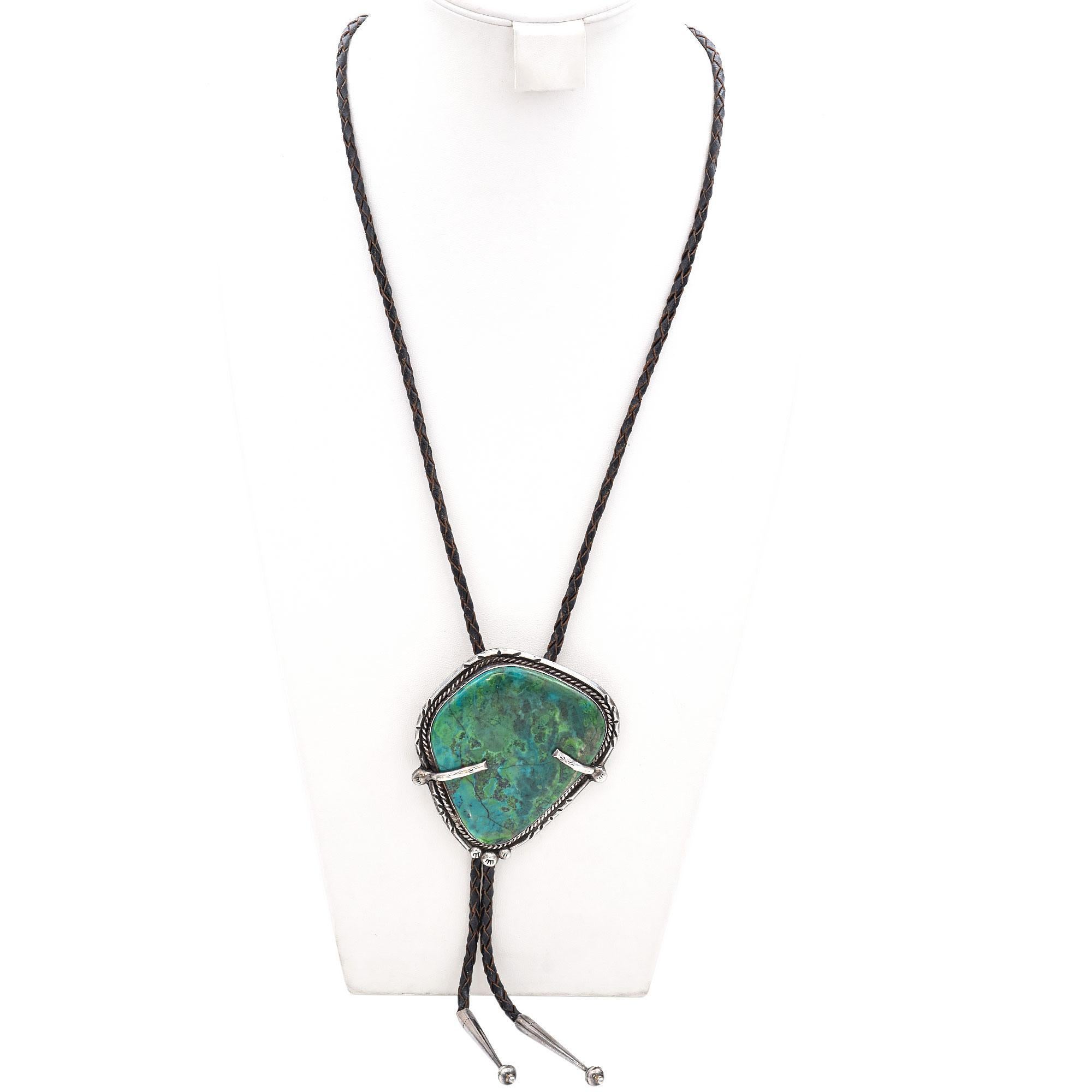 This stunning turquoise bolo tie features a beautifully cabochon-cut turquoise stone in captivating blue and green hues. The stone is set in sterling silver, showcasing exquisite intricate detailing. Bennett has been credited with designing and