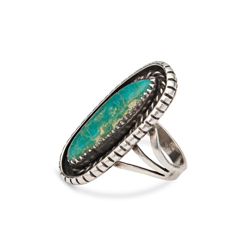 This vintage sterling silver ring features an elongated turquoise stone accented by intricate silver work and set on a triple shank band. It is a size 5.75 but can be resized for a small fee. This ring is 1.25