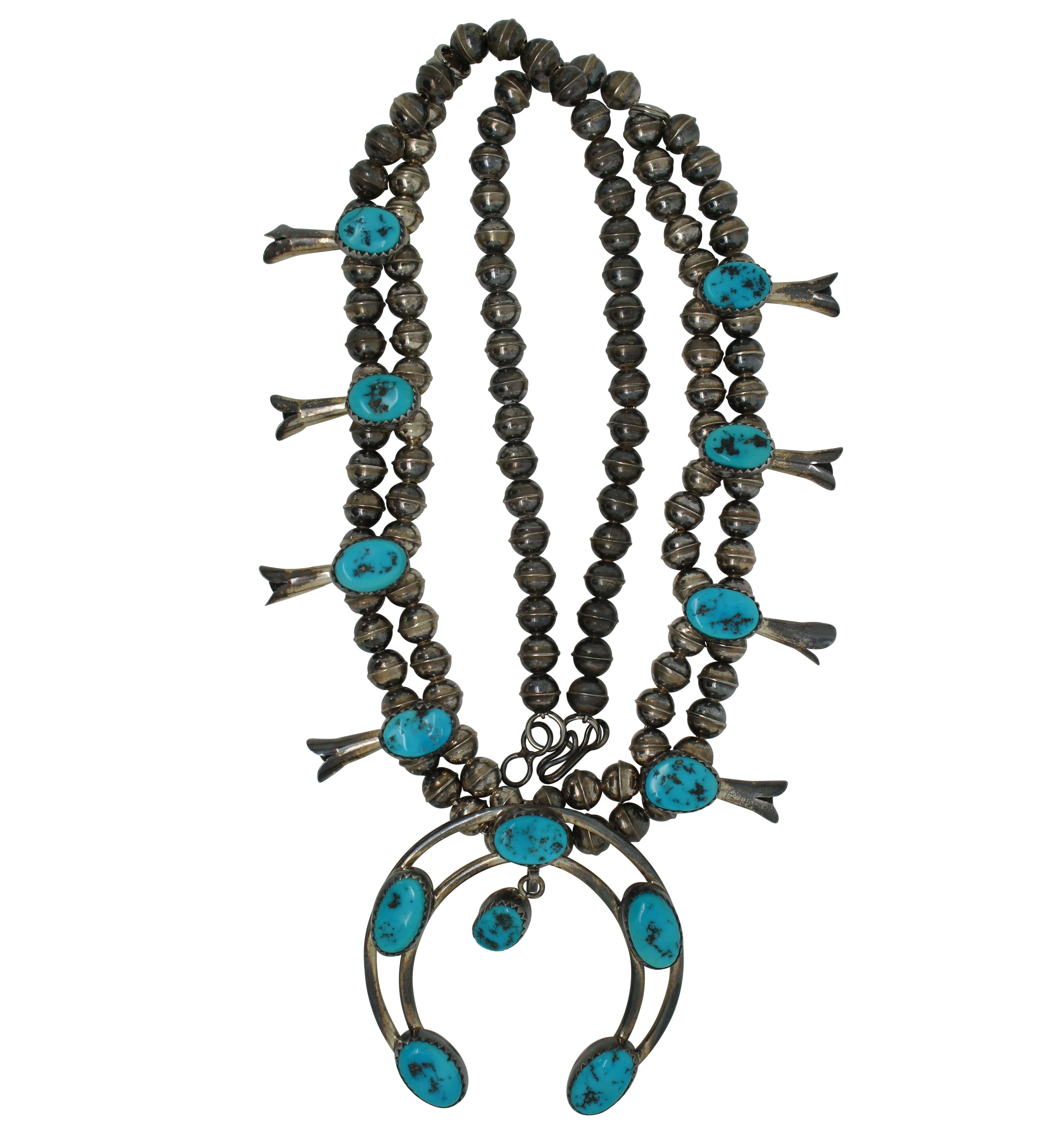 Vintage sterling silver and turquoise necklace featuring a double beaded chain accented with eight oval stones and squash blossom shaped drops, and a crescent moon shaped pendant set with five stones plus one dangling from the center. Paired with