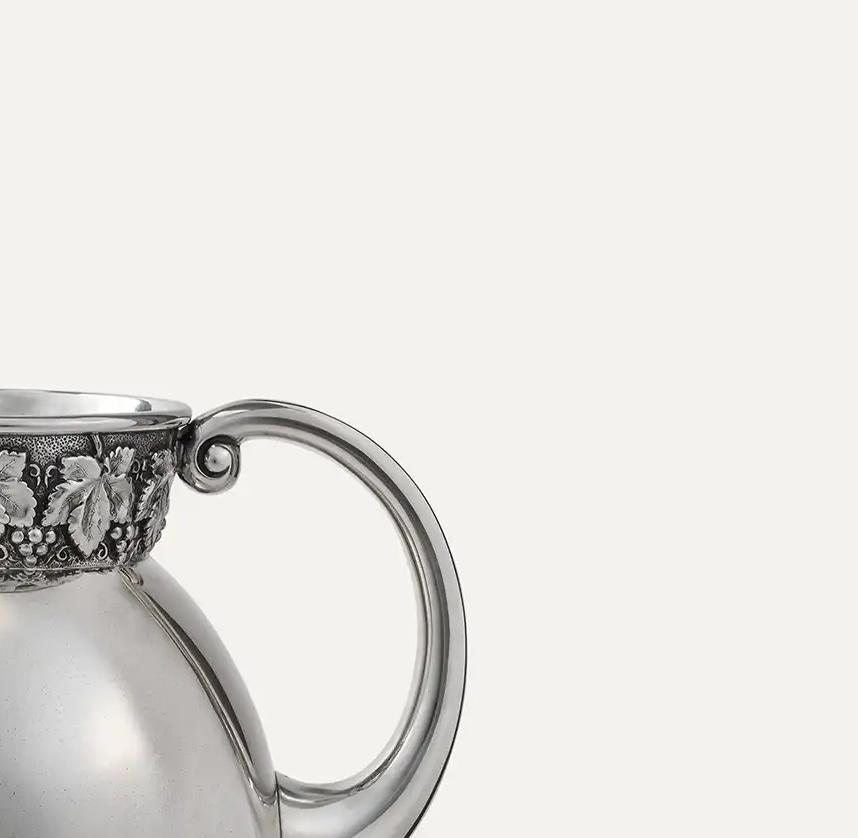 This Antique Portuguese Sterling Silver Water Pitcher is a striking example of early 20th-century craftsmanship, combining artistic refinement with historical authenticity. Meticulously handcrafted in 833 silver, the pitcher is richly adorned with a