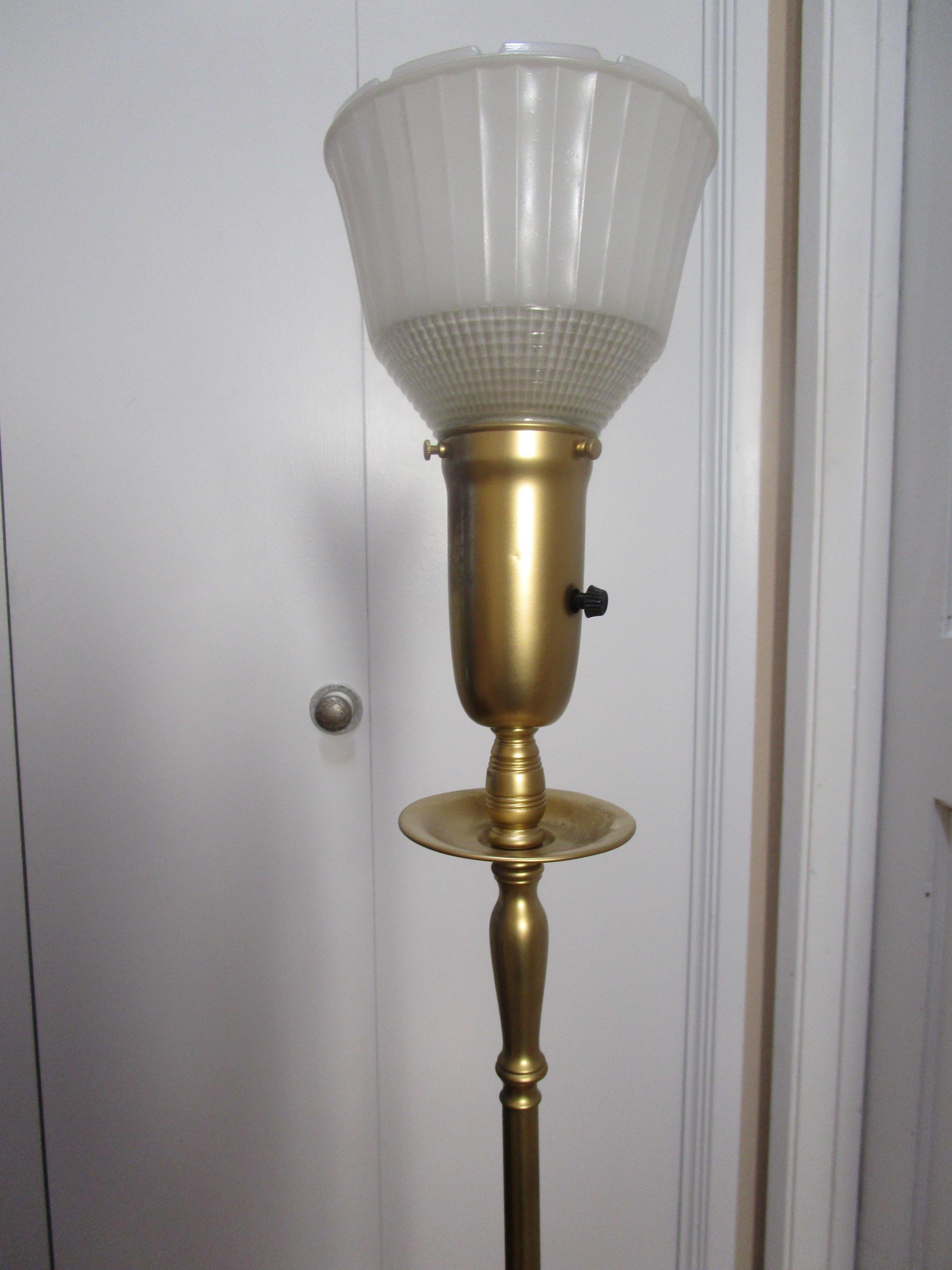 A mid-century modern Stiffel lamp is perfectly balanced on a square base that has four little ball feet. It has most of the weight in the base. It emits a soft light through the torchiere shade. It is on a two-way switch. The lamp is functional and