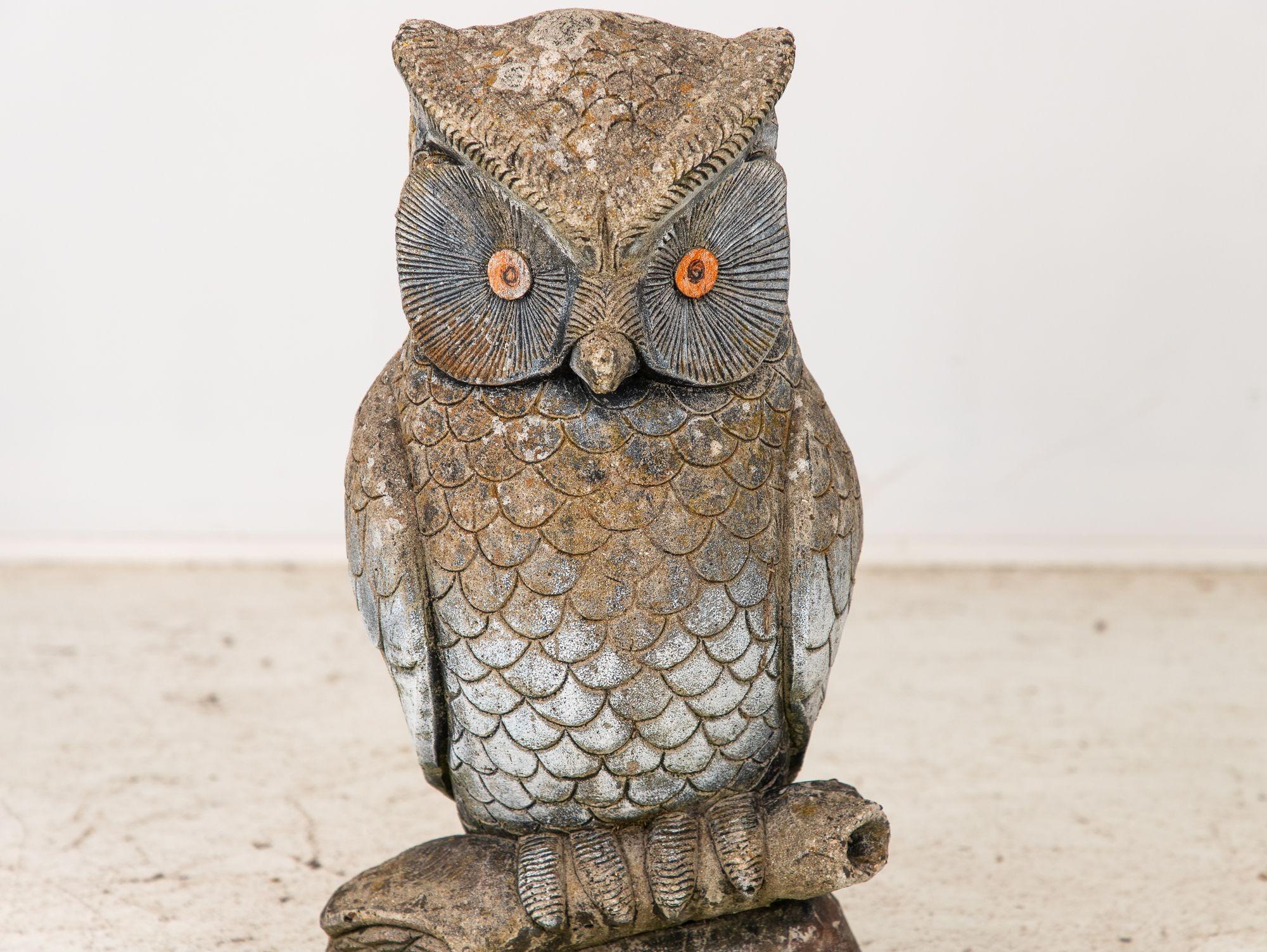 This mid 20th-century French reconstituted stone owl, gracefully perched upon a tree branch, stands as a captivating garden ornament. Remnants of white paint on some feathers and black and orange paint around the eyes bring the ornament to life. Its