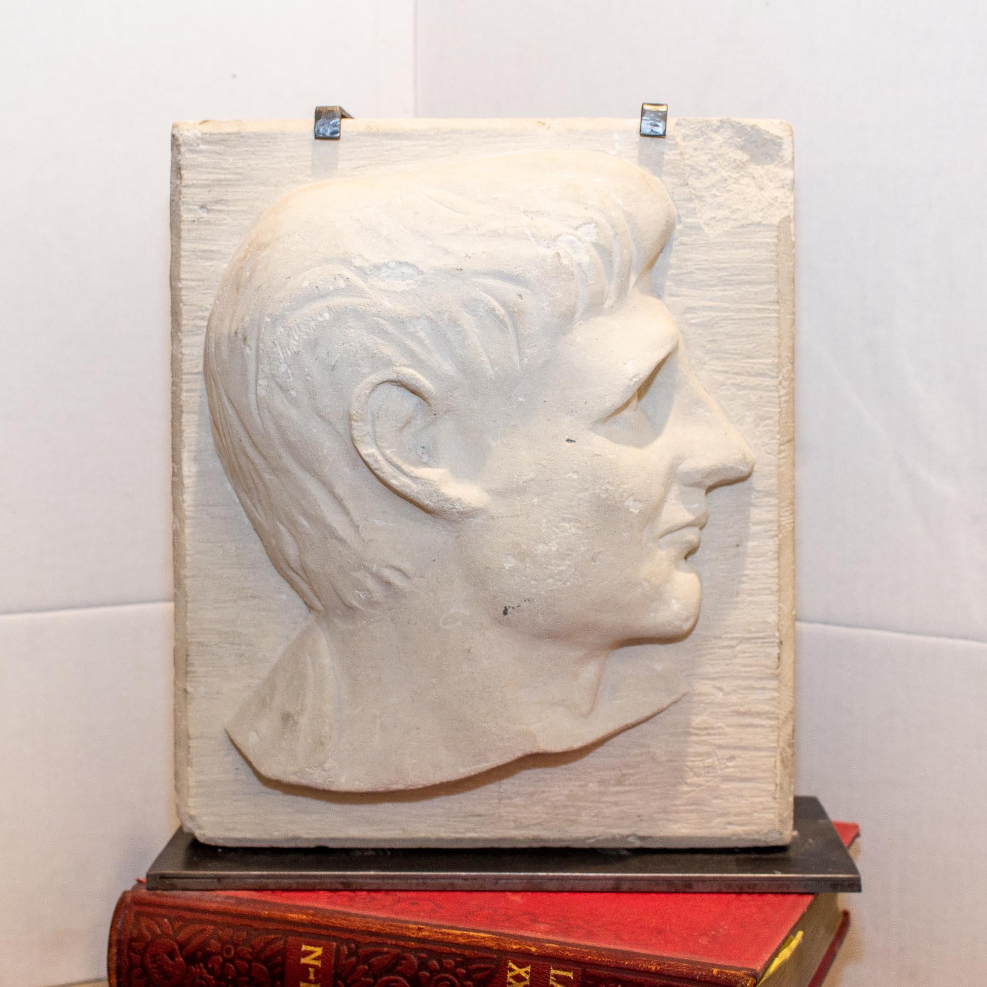 This vintage stone relief features a man's portrait and has been carved into heavy stone (appears to be limestone) and mounted on a custom iron stand. The iron stand was produced in 2019, but the stone piece is vintage. The piece is signed 