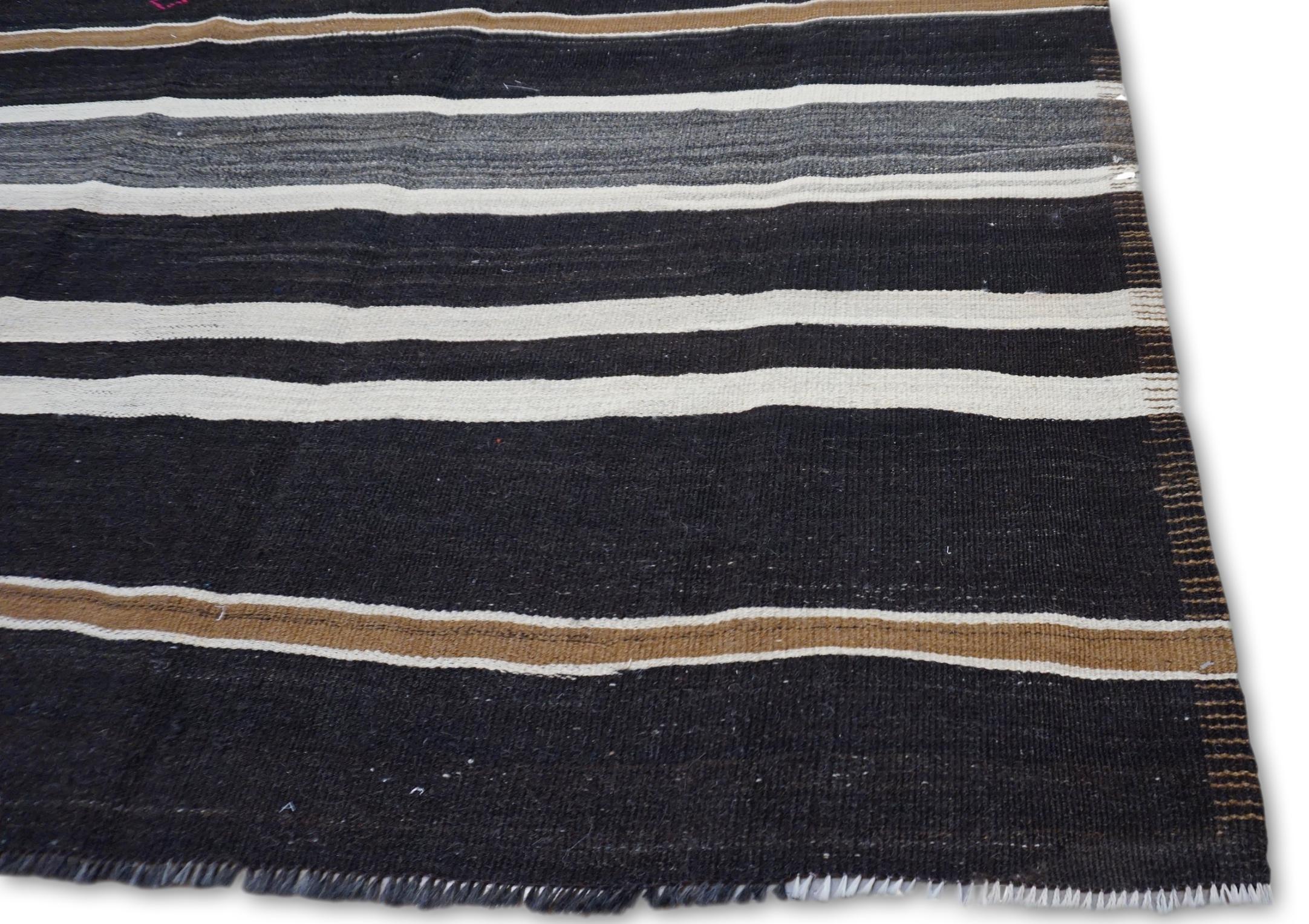 Dieser auffällige Vintage  Der Kelimteppich aus Wolle zeichnet sich durch eine kühne, lineare Komposition aus abwechselnden Streifen in Grau-, Weiß- und erdigen Brauntönen aus, die durch einen anthrazitfarbenen Hintergrund akzentuiert werden.