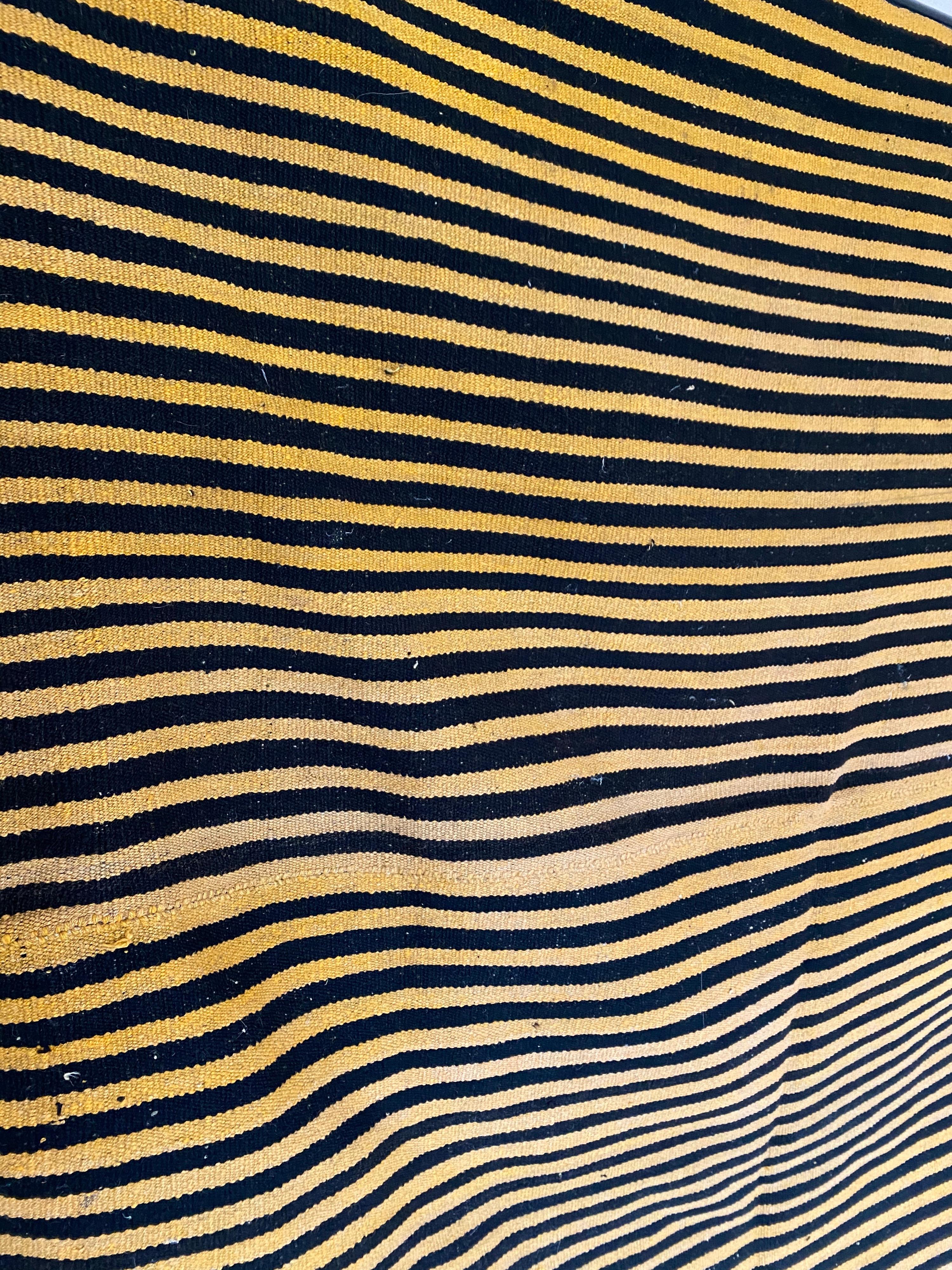 A vintage striped Kilim rug in handwoven wool. Features thin striped bands of golden yellow and black. 
  