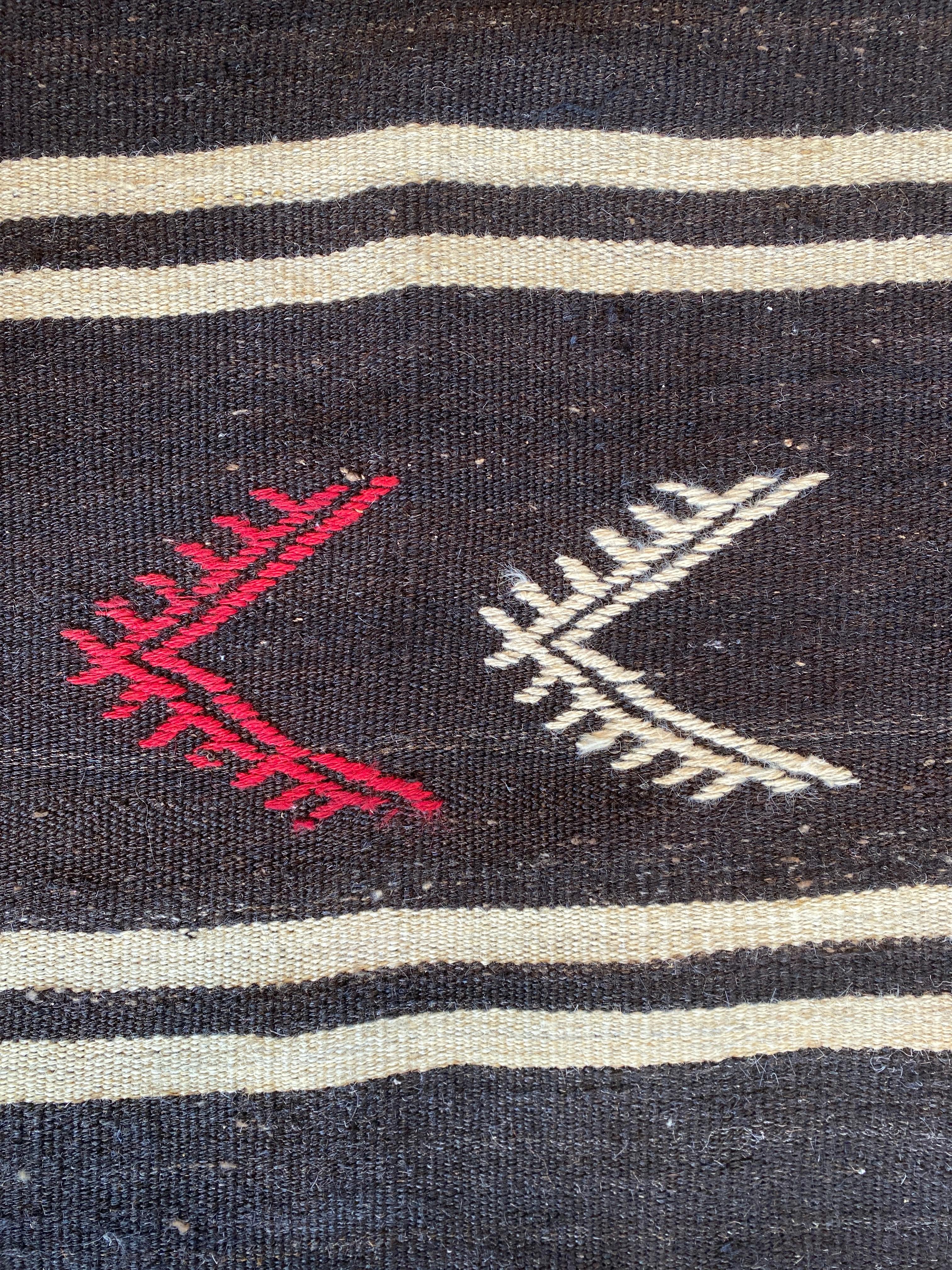 Vintage Turkish Kilim

Circa 1950

Flatweave, good condition. Dark charcoal brown, almost black with pale cream stripes and red, white and turquoise symbols. The hook and evil eye design symbolize protection.

Wear notes: none

Wear