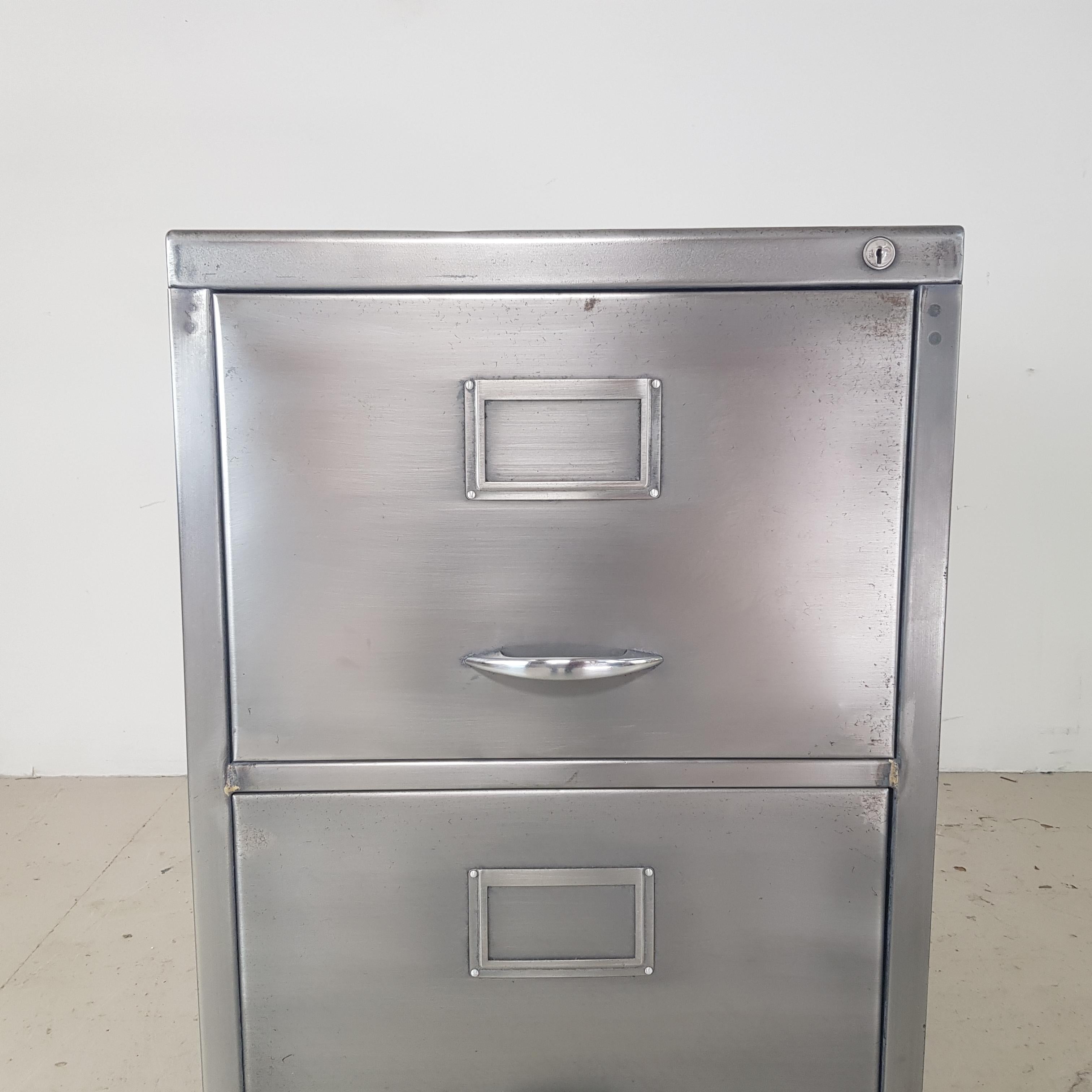 Vintage stripped and polished steel 2-drawer filing cabinet with metal handles. 

The interior is in its original finish. As it's a vintage piece, coming from a working environment, there are signs of wear and tear - a few scratches, scuffs and