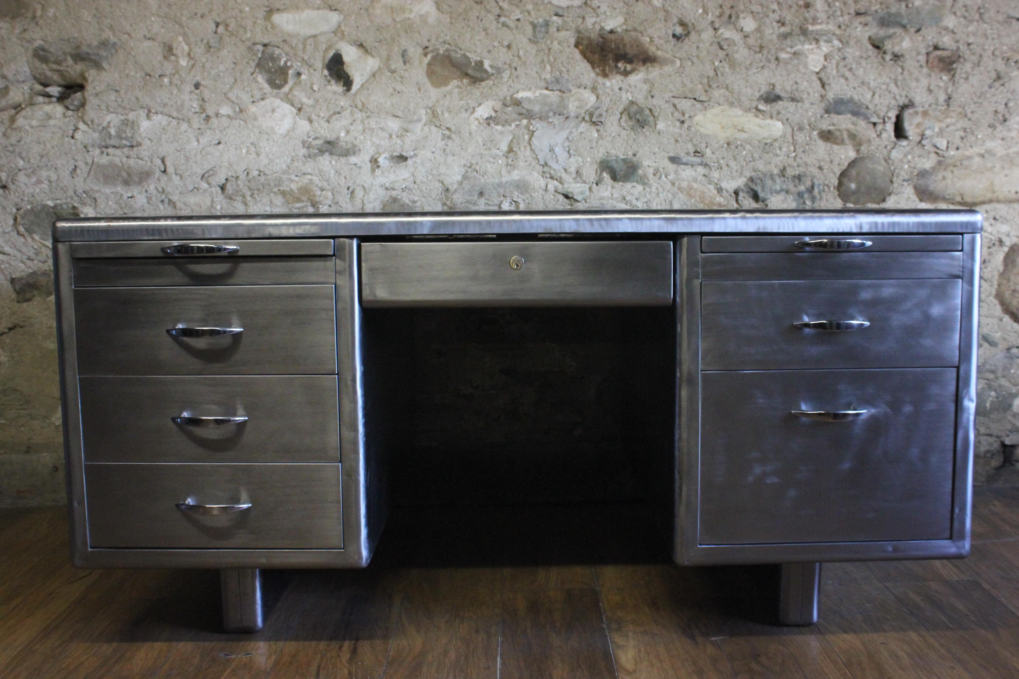 A stunning vintage English stripped metal Art Deco style tanker desk from the 1940s. It has three drawers on one side, two drawers on the other, a centre drawer and two pullout / pull-out shelves which all run smoothly. It has been stripped back to