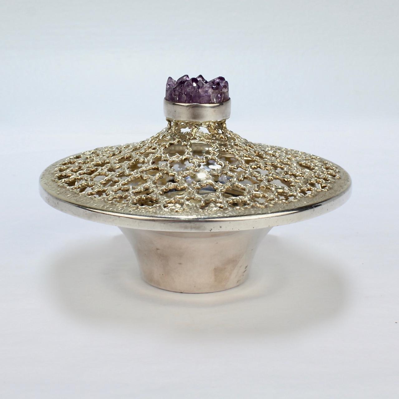 A wonderful Stuart Devlin covered posy bowl.

Comprised of sterling silver with a composite amethyst finial. 

The reticulated top is parcel gilt.

The base is marked for Stuart Devlin, London, 1978, and sterling.

Diameter: ca. 4 1/4 in.

Items