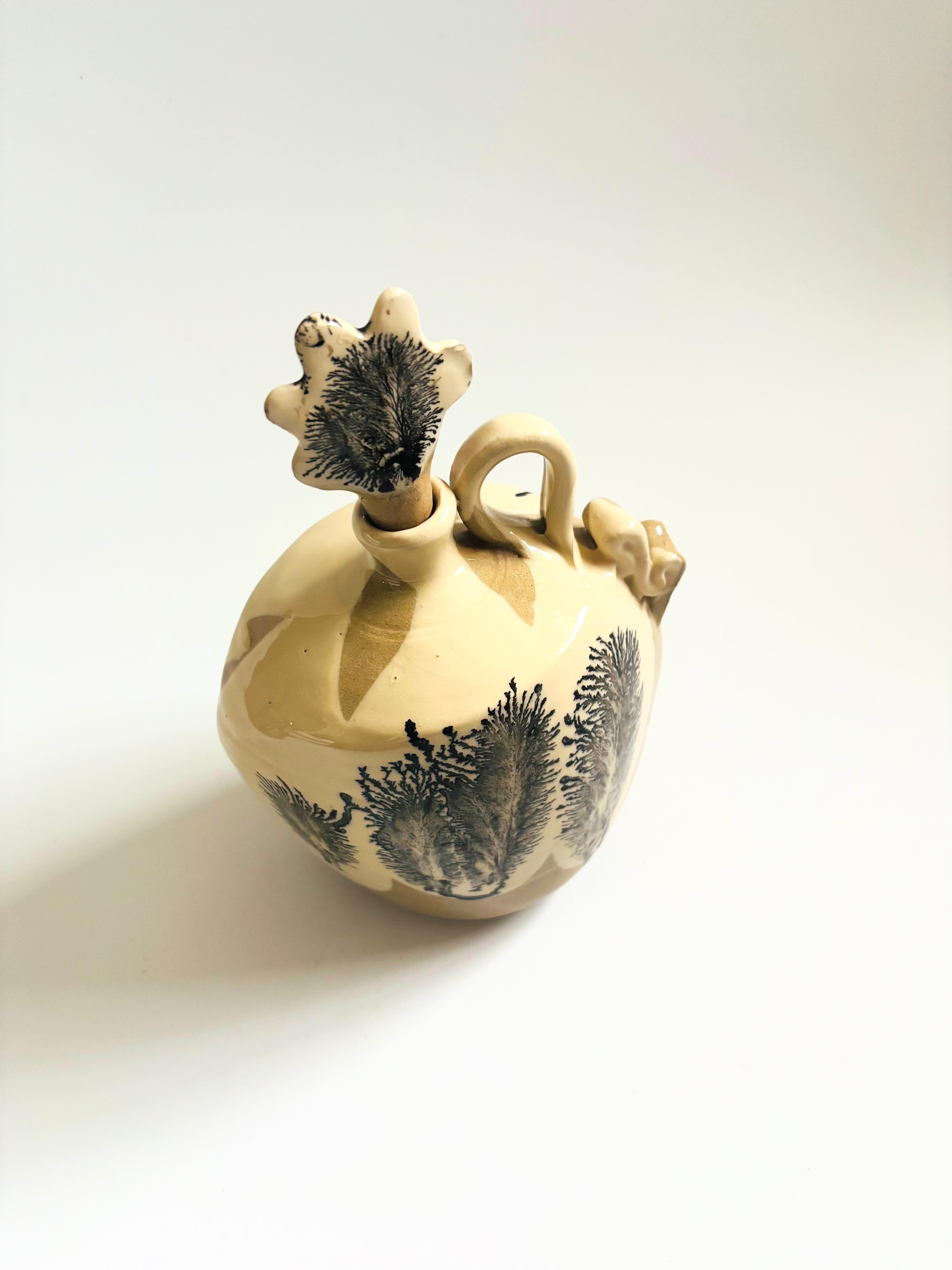 Eine Studio-Keramik-Karaffe im Vintage-Stil. Hellbraune Grundglasur mit einem schwarzen Blattmuster an den Seiten. Abgerundet wird das Ganze durch einen passenden Stopfen. Einzigartiges Banddesign am Griff. Auf dem Sockel vom Hersteller gestempelt.

