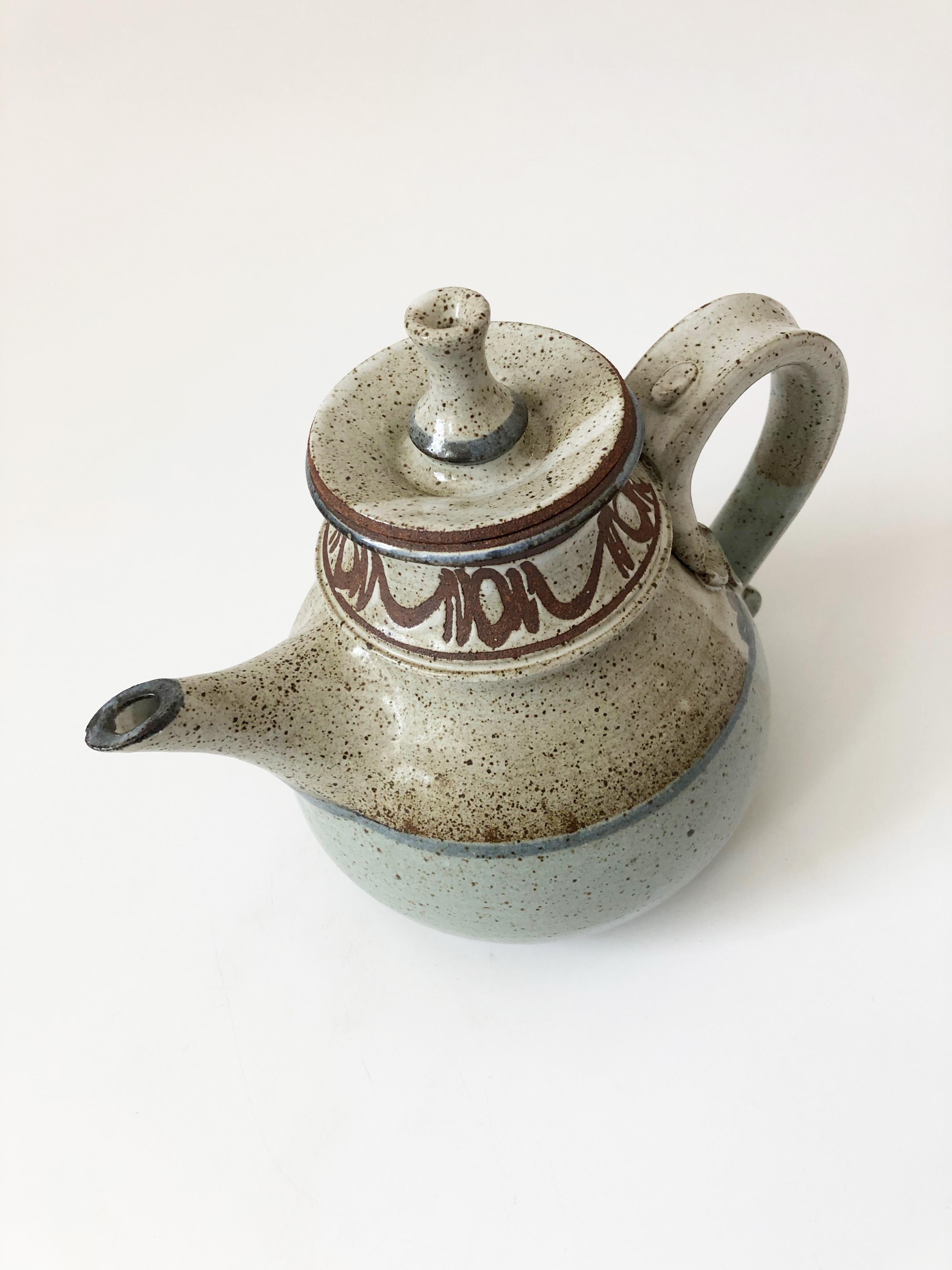 A beautiful vintage studio pottery teapot by pottery, Frank Massarella, of Ojai, California. Features earthy speckled glazes in pale blue and gray with handpainted detailing around the top. Great attention to detail along the side handle and with a