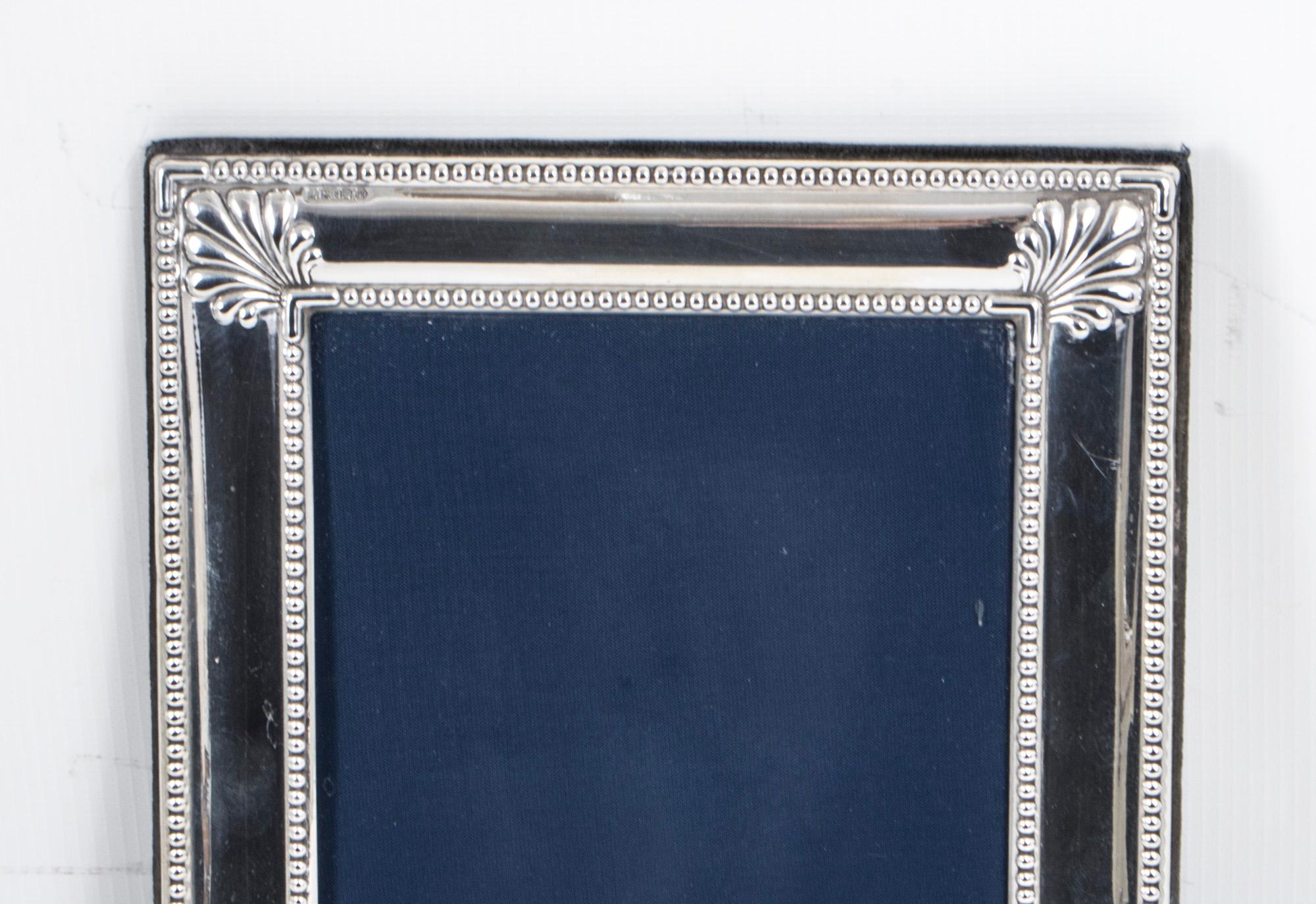 A truly superb medium size Neo classical style photo frame in sterling silver.

Hallmarked for London 1993 with the silversmith's mark for Richard Comyns. 
The vertical frame has a blue velvet back and has a beaded bordered with shell motifs to