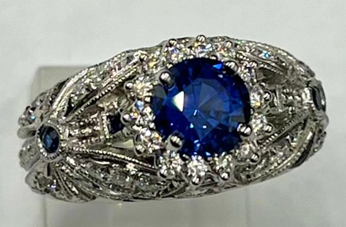 This is a vintage/antique style ring set with a rich, royal natural Blue Sapphire of 1.36Ct.  The ring is hand carved and has delicate and intricate detail with great craftsmanship. The Sapphire is surrounded by a halo of diamonds which then blends