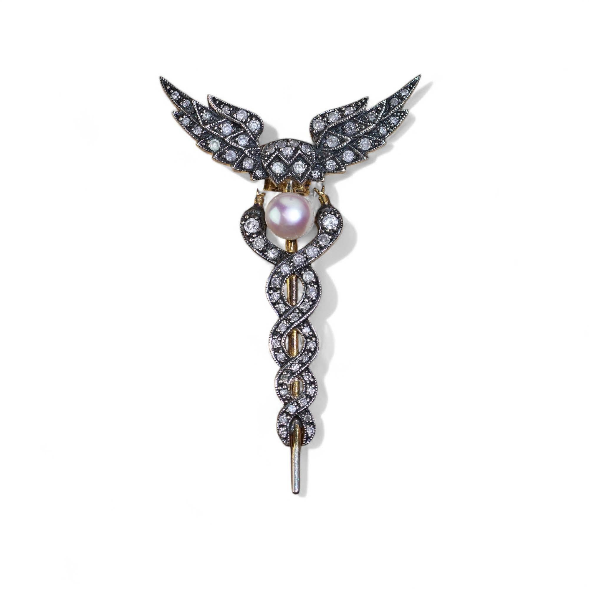 Spilla Caduceo in stile vintage in oro e argento 9kt, con perla coltivata e 0,48 carati di diamanti a taglio rotondo. Ispirato alla mitologia greca, elegante e da collezione.

Dimensioni e peso
Lunghezza: 4.8 cm
Larghezza: 3,0 cm
Diametro della
