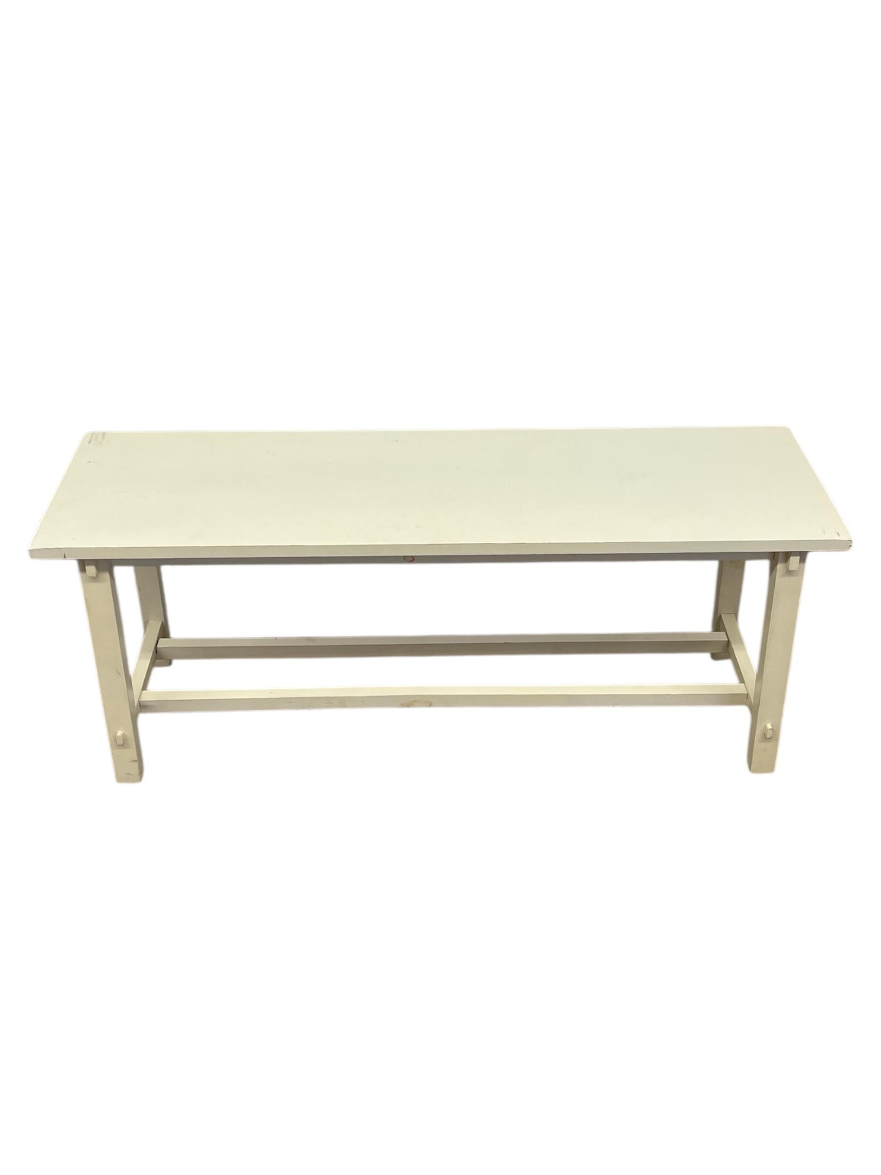 Tavolo o panca da cascina in stile vintage con piano rettangolare allungato e base a traliccio. La finitura è in un tenue tono crema, che mostra un'usura adeguata all'età che ne aumenta il fascino utilitaristico. Il design è semplice e funzionale,
