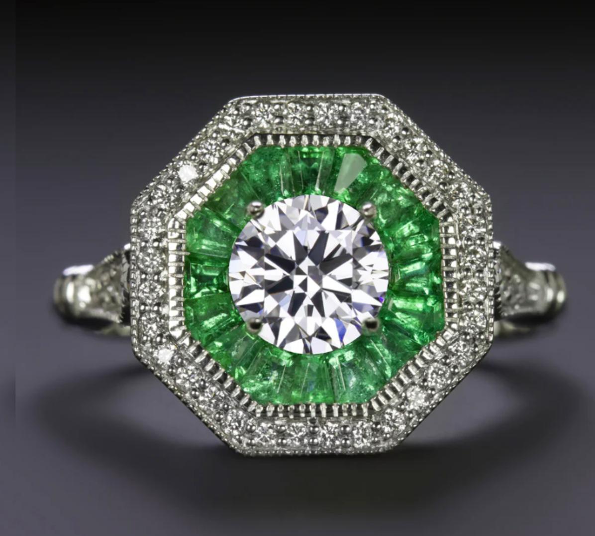 Questo squisito anello di ispirazione Art Déco mette in mostra un diamante brillante di taglio rotondo al centro, circondato da una doppia aureola ottagonale mozzafiato di smeraldi verdi e diamanti abbaglianti. Un capolavoro davvero elegante e senza