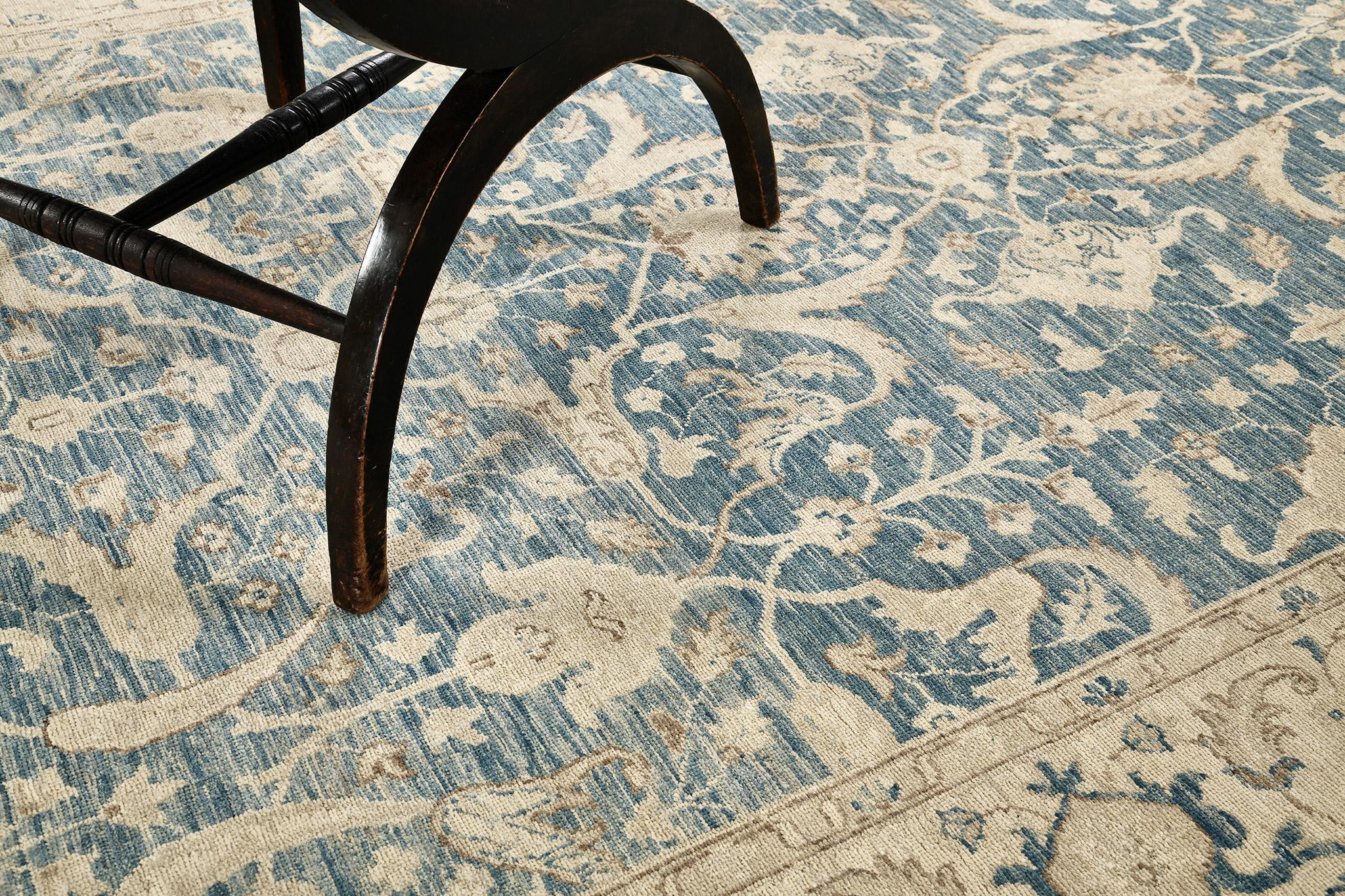 A sophisticated pile woven wool rug revival from Raptured Collection that features ash gray symmetrical floral scrolls and spiral vines in a sky blue field with a hint of gold in its outline. It defines its uniqueness and glamour to match your