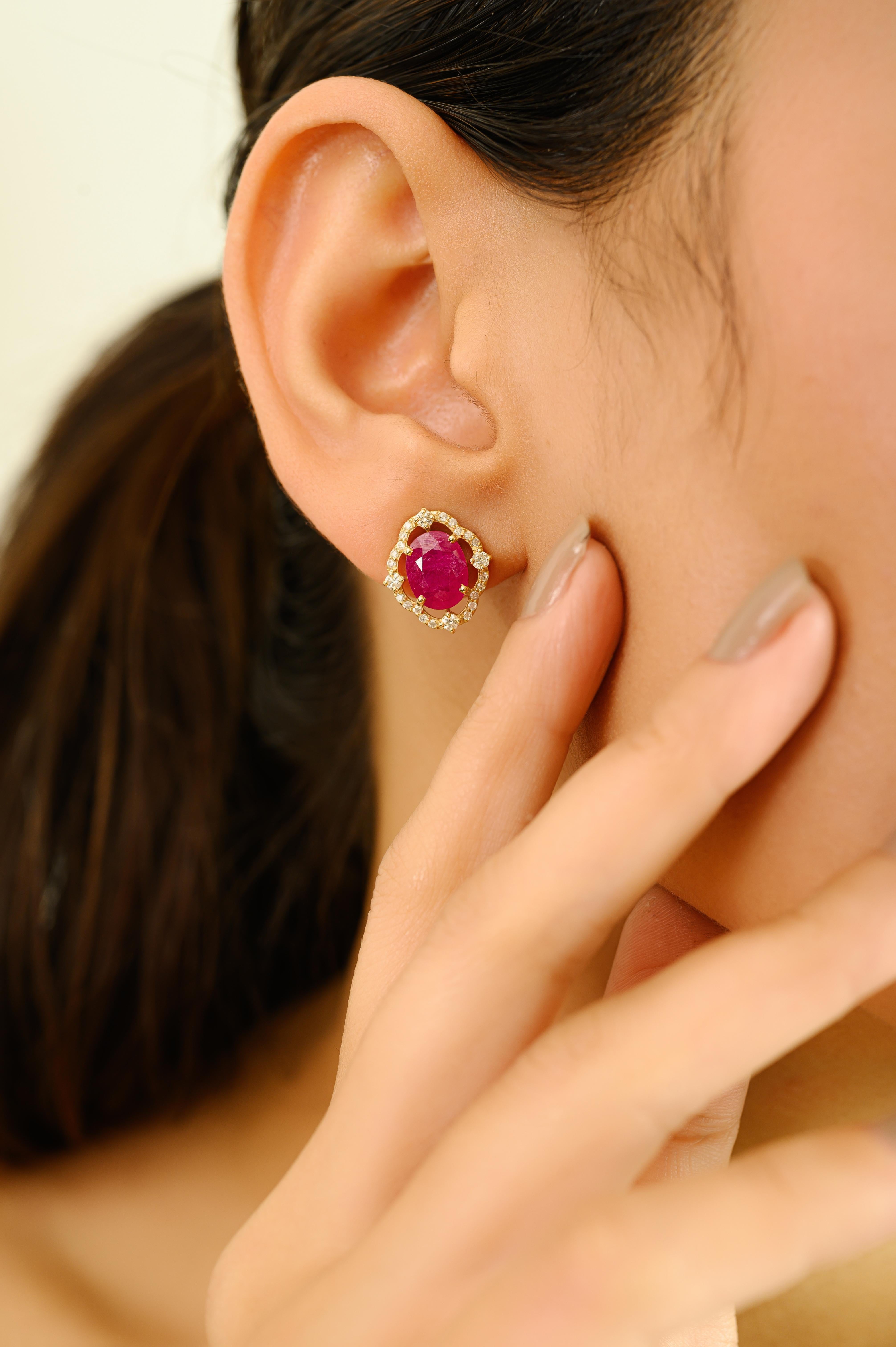 Elegant and timeless, these exquisite earrings are crafted in 14k yellow gold and feature vibrant oval-cut rubies totaling 3.85 carats. Each ruby is encircled by a delicate scalloped halo of sparkling diamonds, weighing a total of 0.49 carats. The
