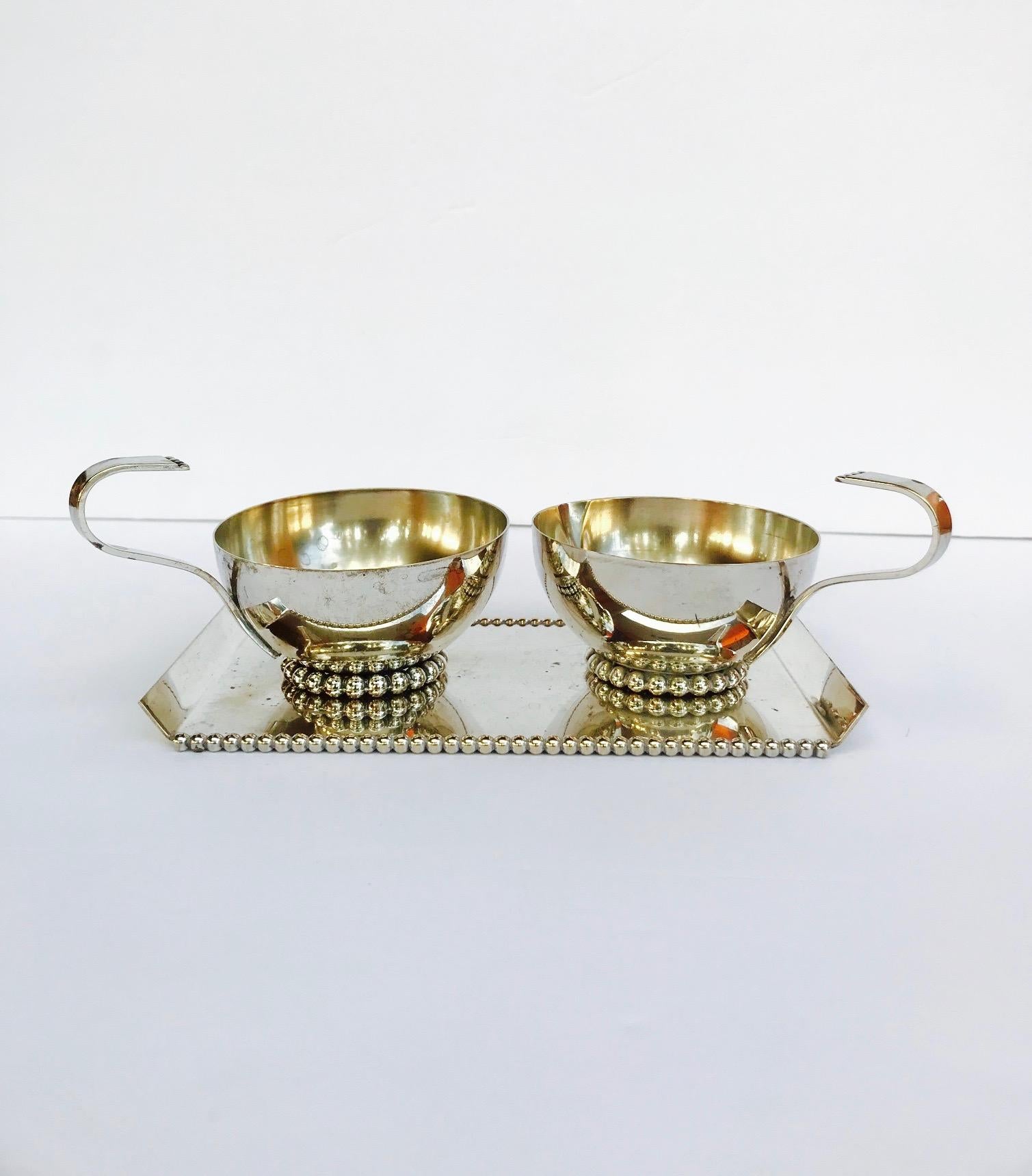 Italian Mid-Century Modern serving set handcrafted from silver plated metal. The set features handled creamer with spout and handled sugar bowl. Both pieces have elegant saucer forms with stylized hand forged handles. 
Modernist serving tray