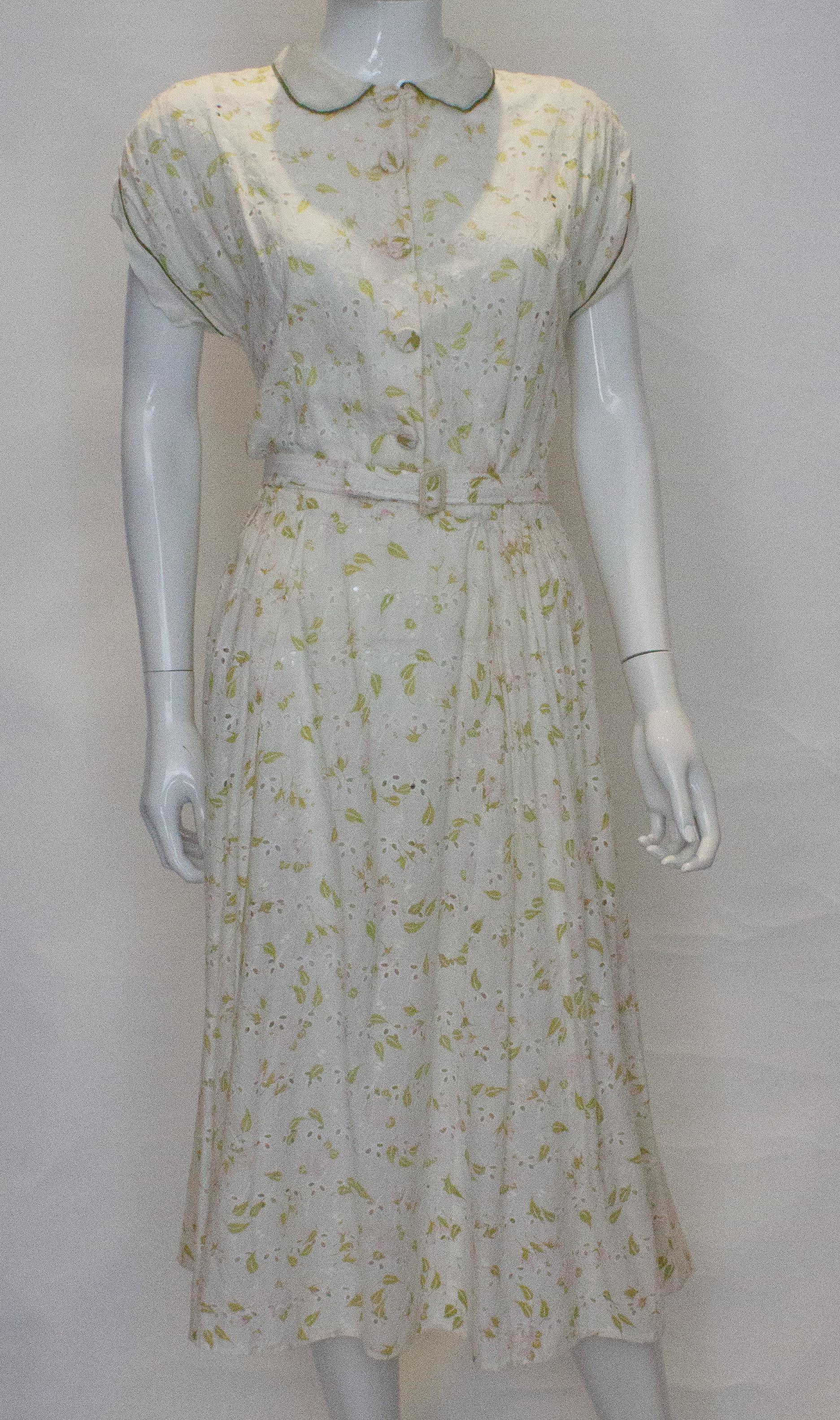 Ein hübsches Vintage-Baumwollkleid von Nelly Don. Das Kleid aus weißer Baumwolle mit rosafarbenen und grünen Details hat einen Rundkragen, eine Knopfleiste, lange Ärmel und einen seitlichen Reißverschluss.