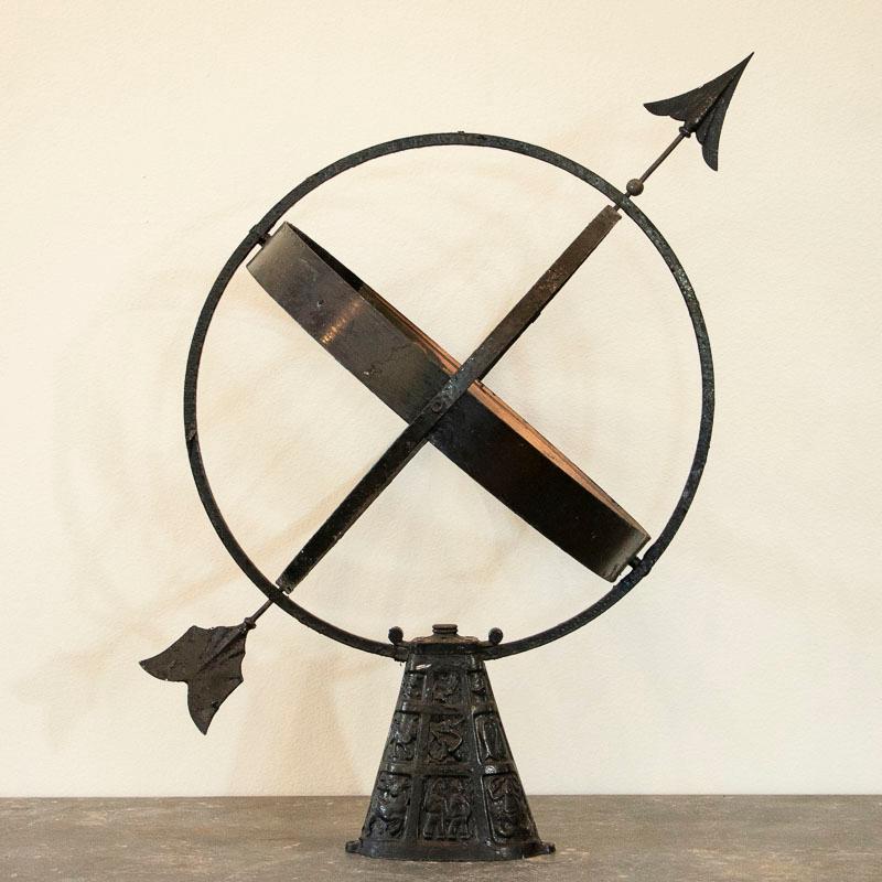 This vintage black painted globe shaped garden ornament, called an armillary, is made up of metal bands, pierced by an arrow and supported by a mounting bracket. The base has images of the zodiac in each of the small panels. These 