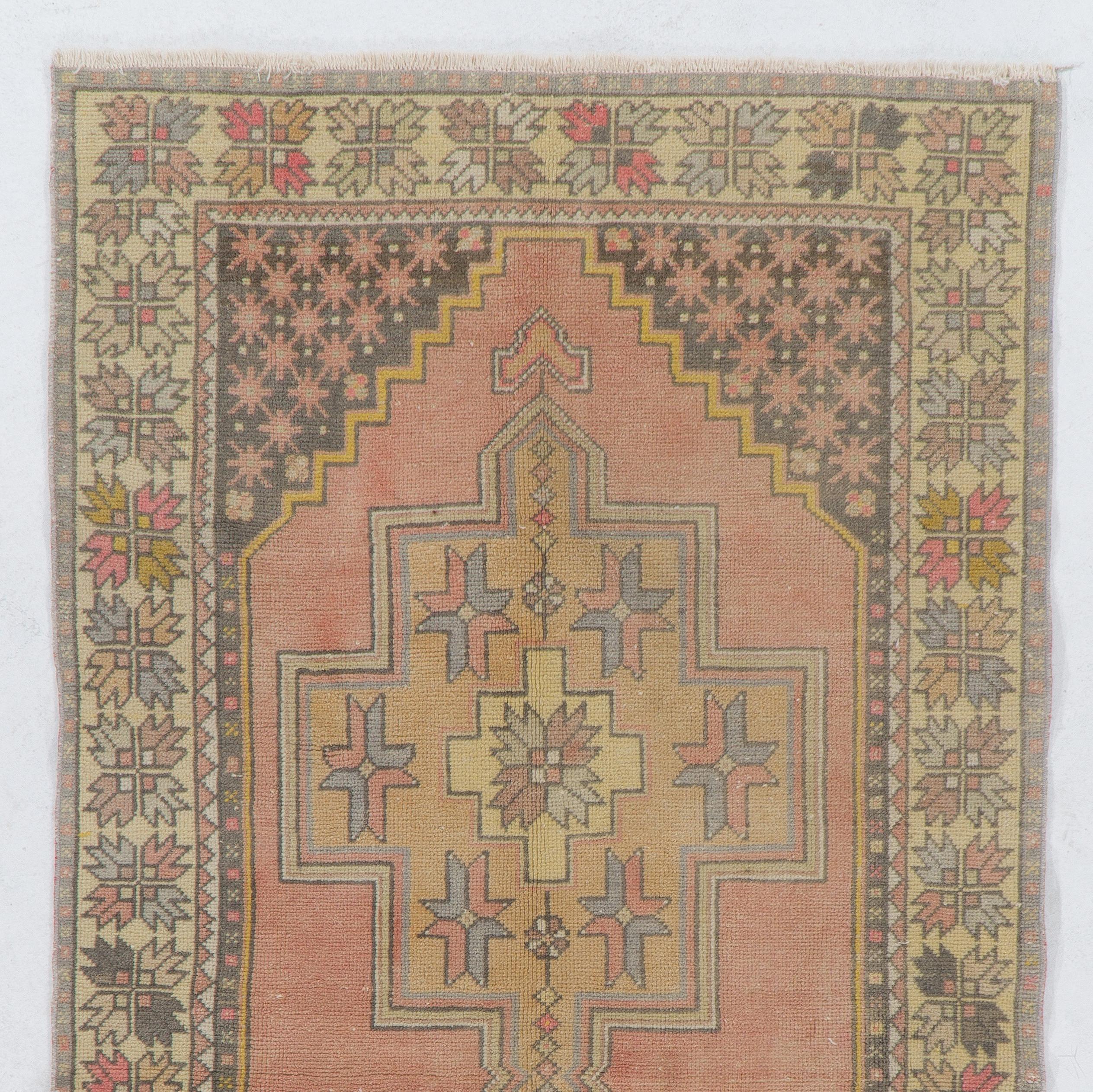 This vintage Central Anatolian rug features two linked medallions in soft tan and gold colors and cross-shaped motifs inside against a plain field in soft muted red. The corner-pieces in charcoal gray are decorated with large, elongated palmettes.