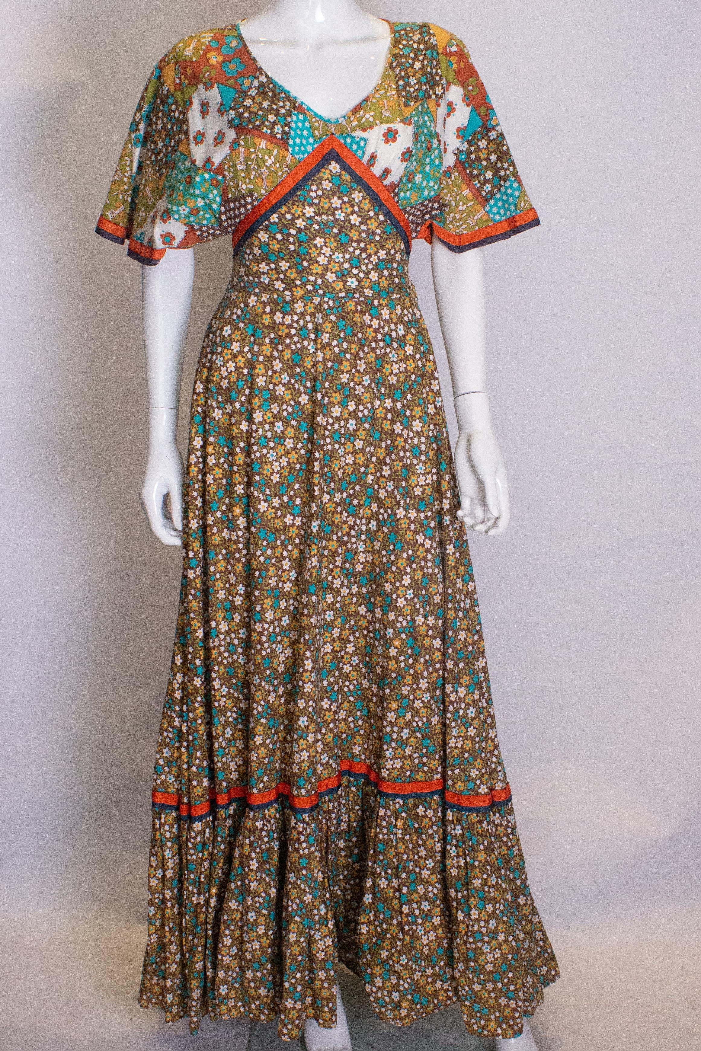 A fun vintage gown by Susan Small.The dress is in a colourful patchwork print, and has a v neckline, cap sleeves, a self fabric tie belt, frill at the hem, and a central back zip.