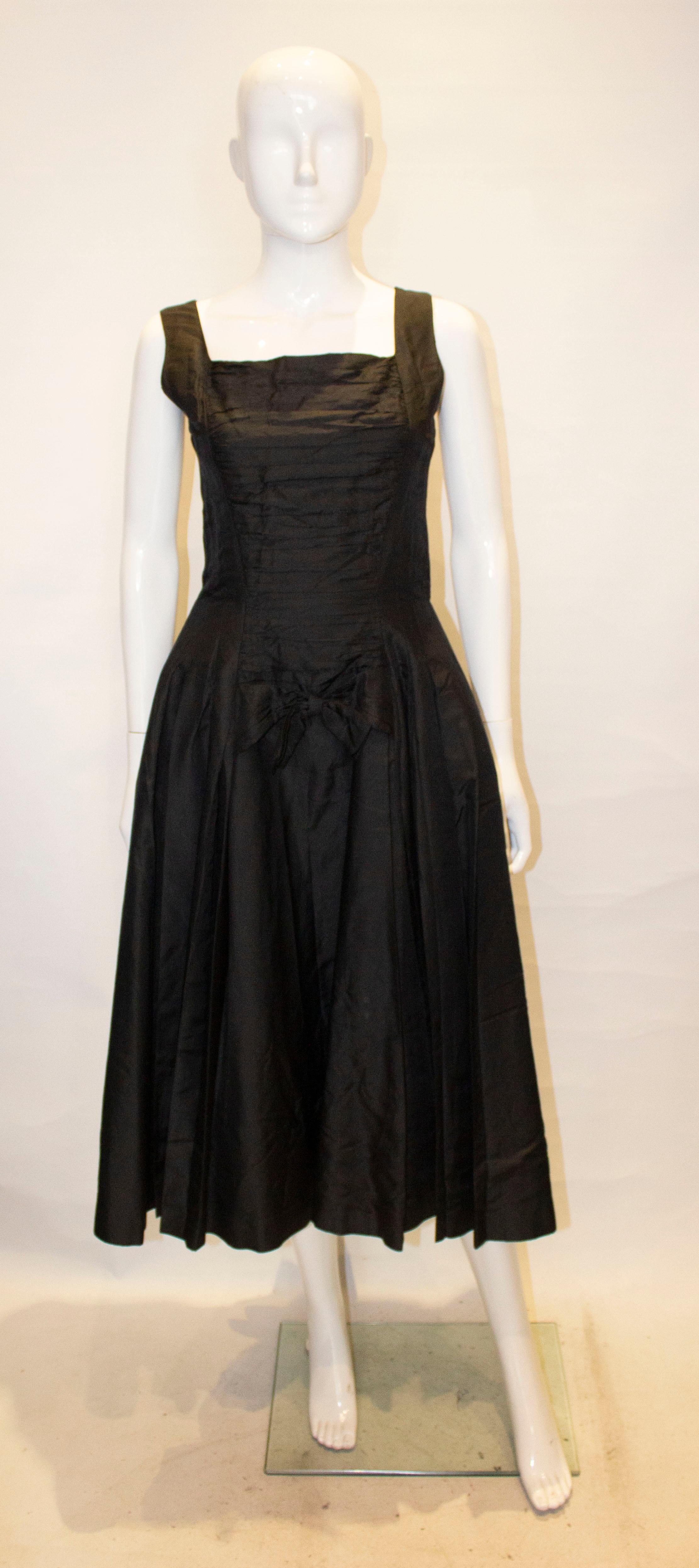 A pretty black cocktail dress by Suzy Perette.The dress has  a square neckline and low backline. It has gathering at the front with a bow detail, a belt at the back and a full underskirt.