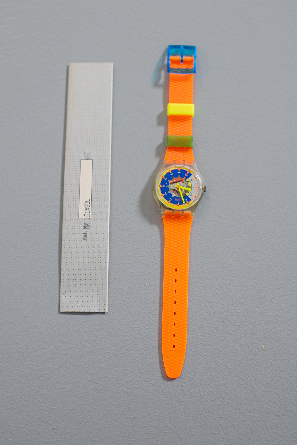 Particular vintage Swatch watch from the 1993 collection. The strap is made of plastic with details that resemble fish scales, the dial has a beautiful graphics with complementary colors, in the center there is a transparent sun in which the gears