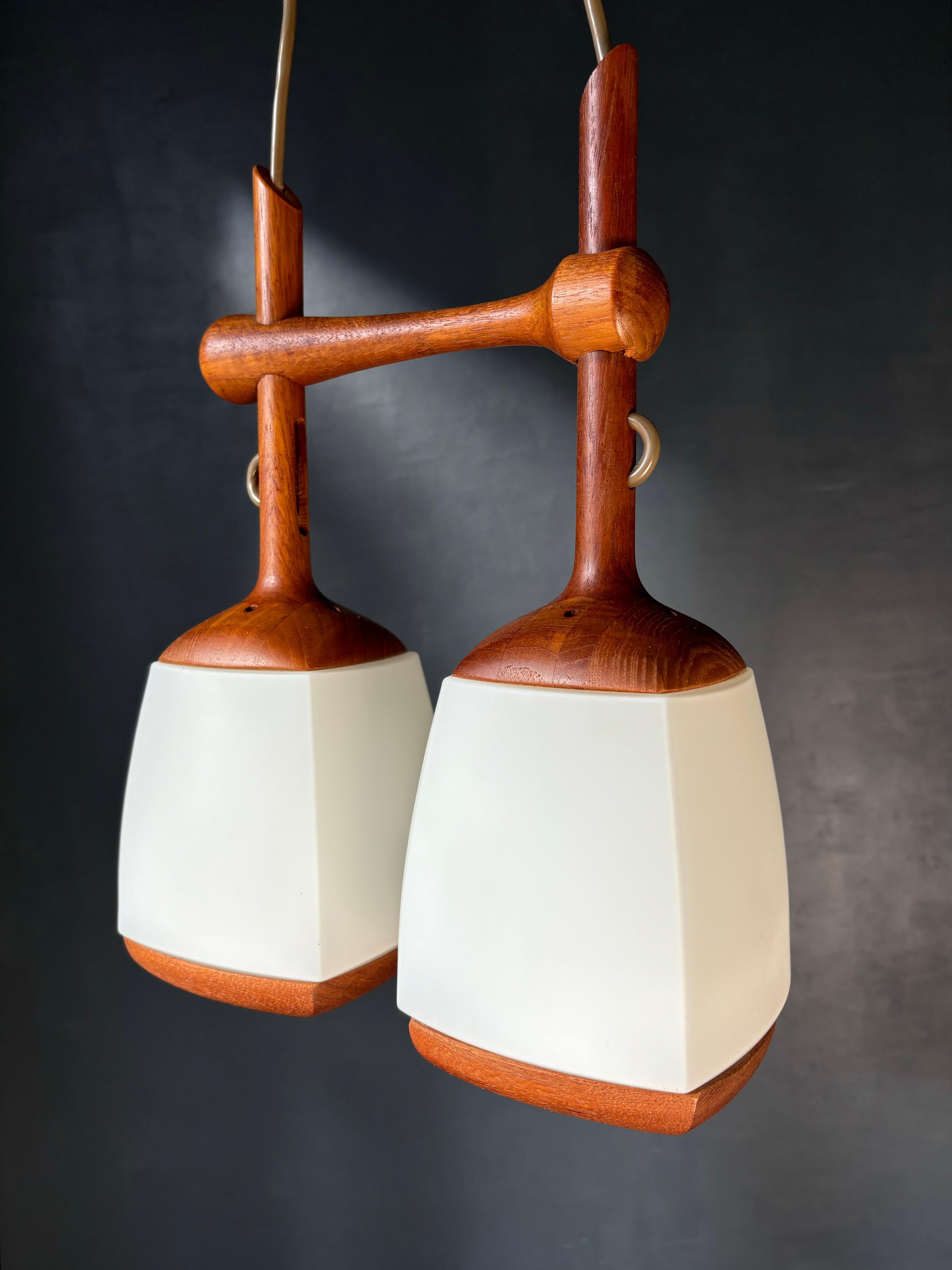 Wooden double pendant manufactured by AB Stilarmatur Tranås in the 1960s. Two slender arms on teak mount with soft angled milky white glass shades. 
Height including wooden canopy 75 cm/29.5 inches - height can easily be adjusted. 
Fittings for