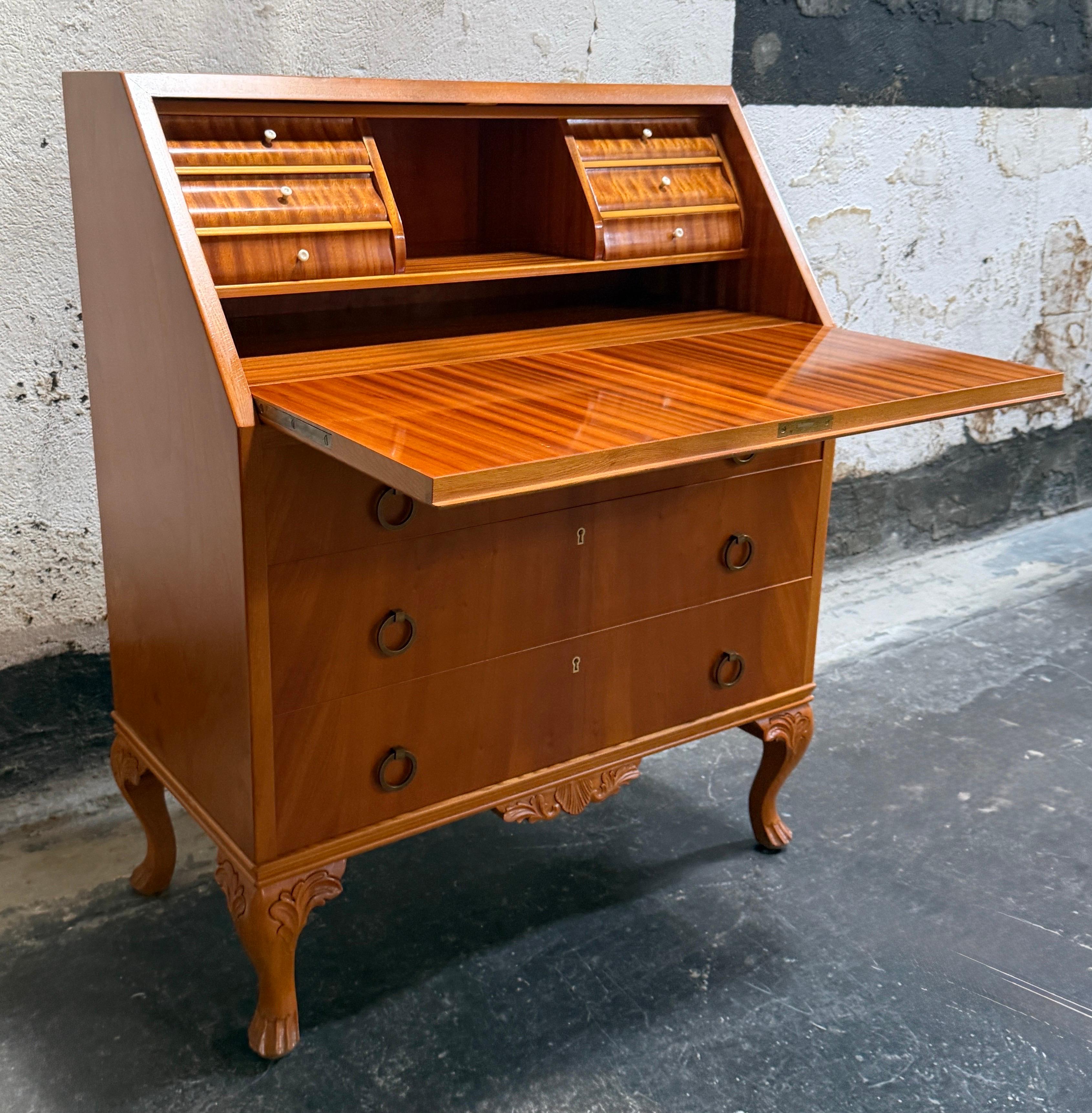Elegante scrittoio secretaire a ribalta realizzato in olmo dorato e mogano con dettagli in olmo intagliato, gambe a cabriole, scanalature in bachelite, tiretti interni dei cassetti in bachelite e tiretti esterni in ottone antico.  Realizzato in