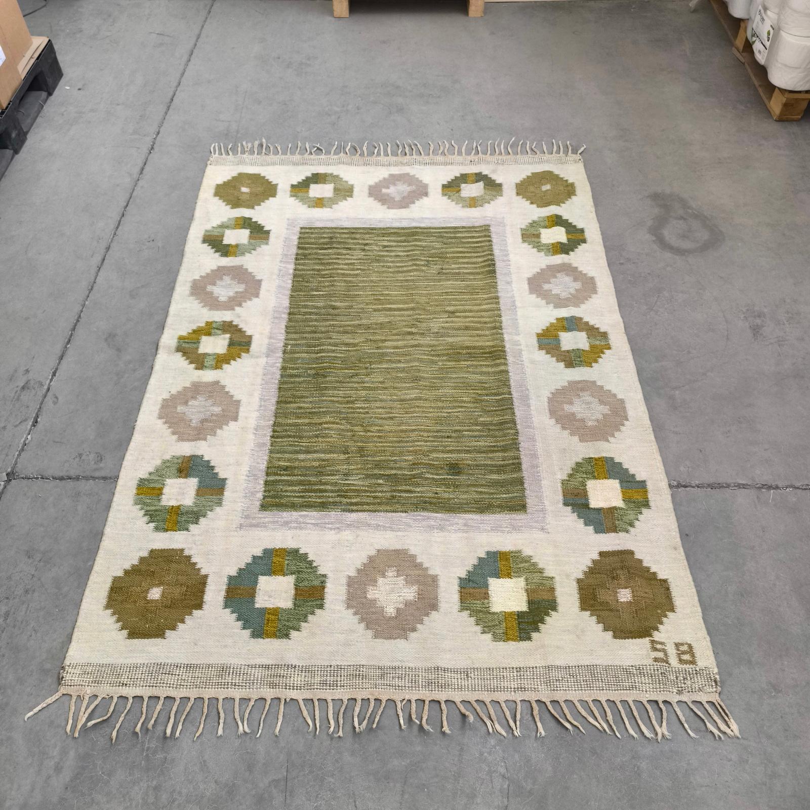 Questo tappeto vintage a trama piatta è stato tessuto a mano in Svezia negli anni Cinquanta.  
Disegnato da Birgitta Södergren. Presenta un motivo geometrico nei toni del verde, del beige e del marrone.
Realizzato con la tradizionale tecnica del
