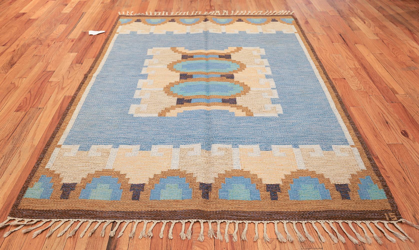 Chic and subdued, this beautiful, artfully decorated signed vintage Swedish Kilim depicts a bold rectilinear centerpiece that is adorned with angular ram's horns and radiant ovoid capsules that are filled with beautifully selected colors. The