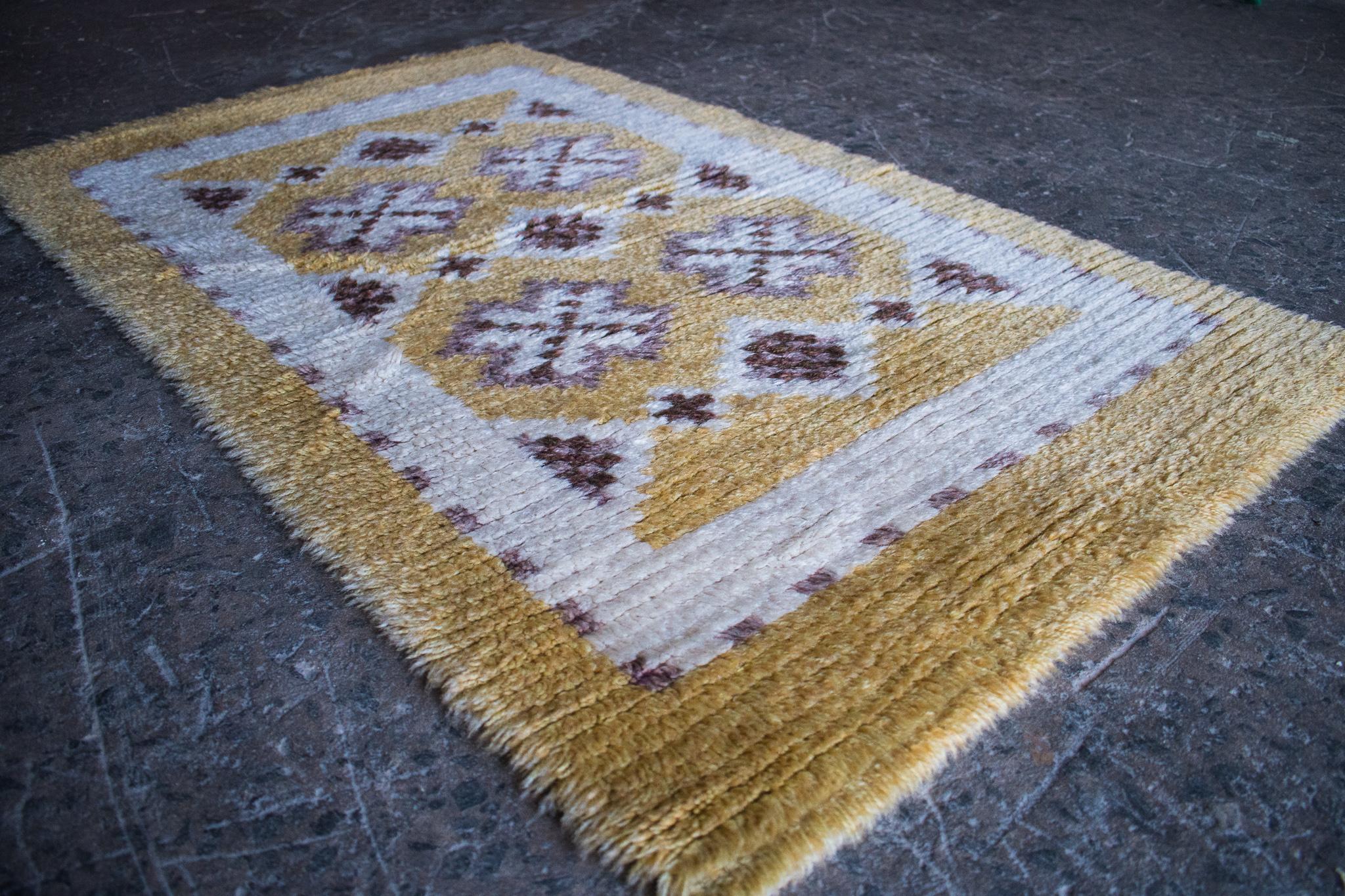 Bright and cheerful Swedish Modern Rya rug. Light gold, cream, lavender, and plum with a geometric pattern. Hand-hooked of wool yarn, this is the perfect petite rug to place by your bedside or layered on a larger rug.