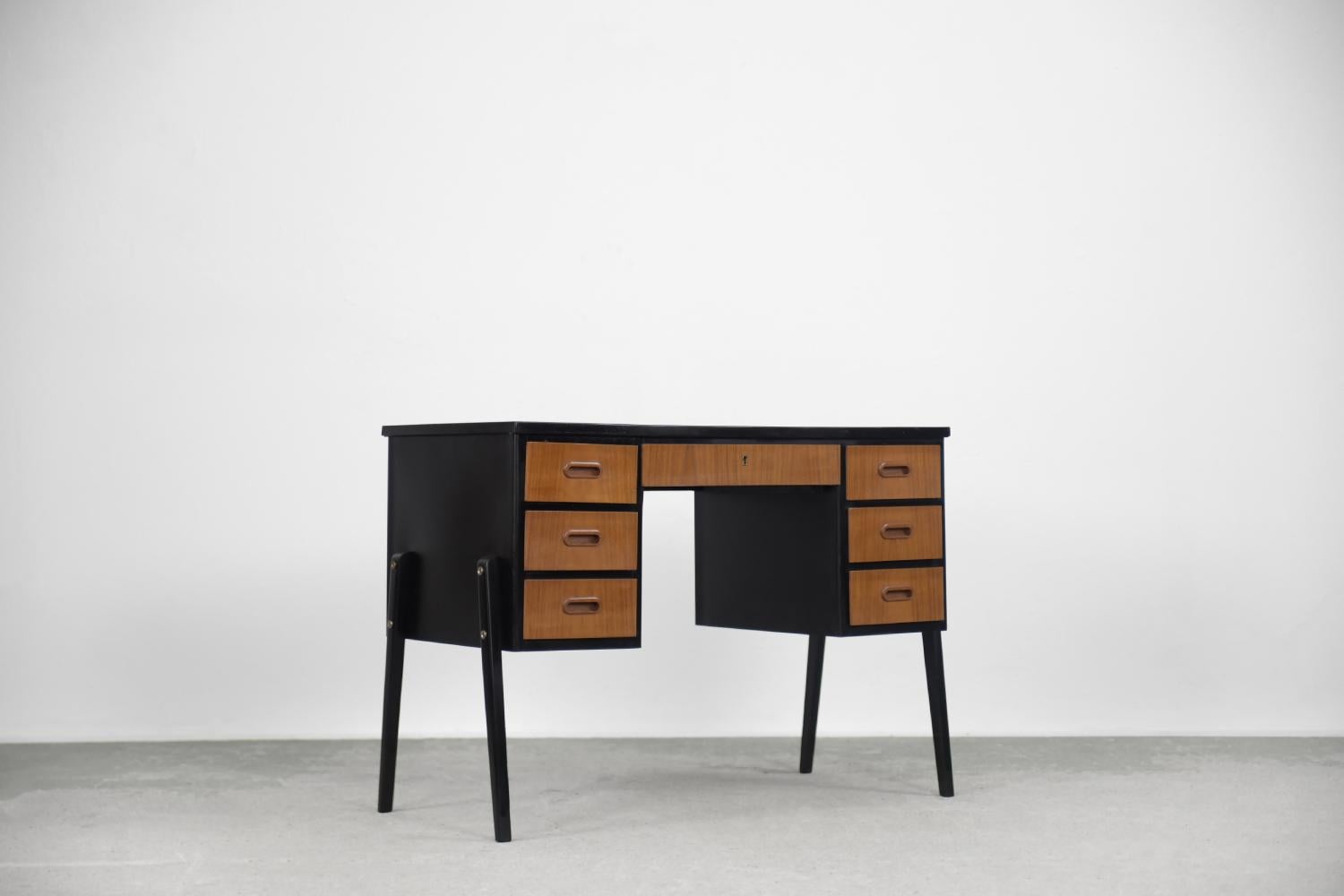 This classic desk was made in Sweden during the 1960s. It is made of brown-gold teak with black elements. Teak wood is very durable, it comes from four types of teak trees. The high content of oily substances means that practically no water soaks