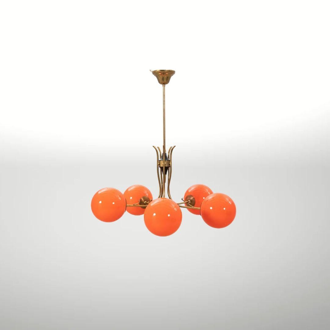 Esta lámpara de araña sueca vintage de los años 70 tiene un aspecto alegre y retro, con cinco puntos de luz, estructura metálica y brillantes pantallas de cristal naranja. Tiene ese aire clásico de mediados de siglo y es una gran pieza decorativa