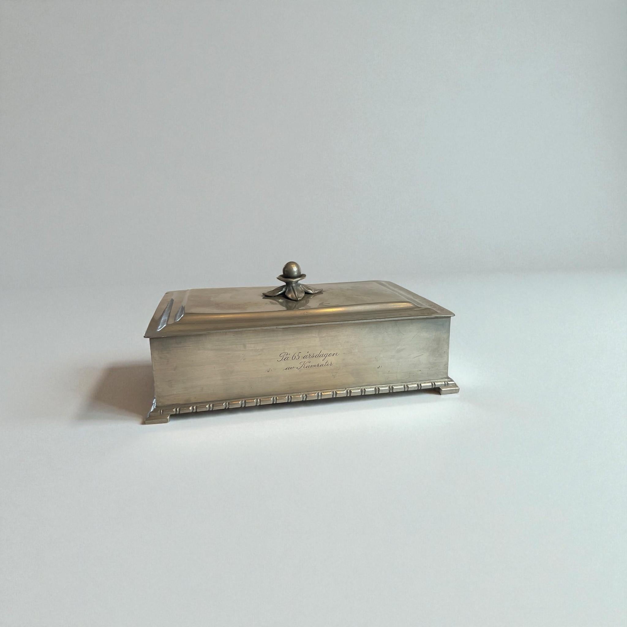 Magnifique boîte à cigares vintage en étain fabriquée par GAB (Guldsmedsaktiebolaget), Suède, 1934. Cette élégante boîte rectangulaire présente des lignes Art déco épurées, un fleuron détaillé sur le couvercle et un intérieur en bois chaleureux.