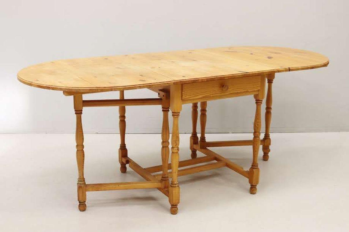 Vintage Swedish pine gateleg dining table. This table top features a fixed rectangular center section and two hinged leaves on either side, which, when not in use, fold down to hang vertically at the sides and below the fixed section. Two of the