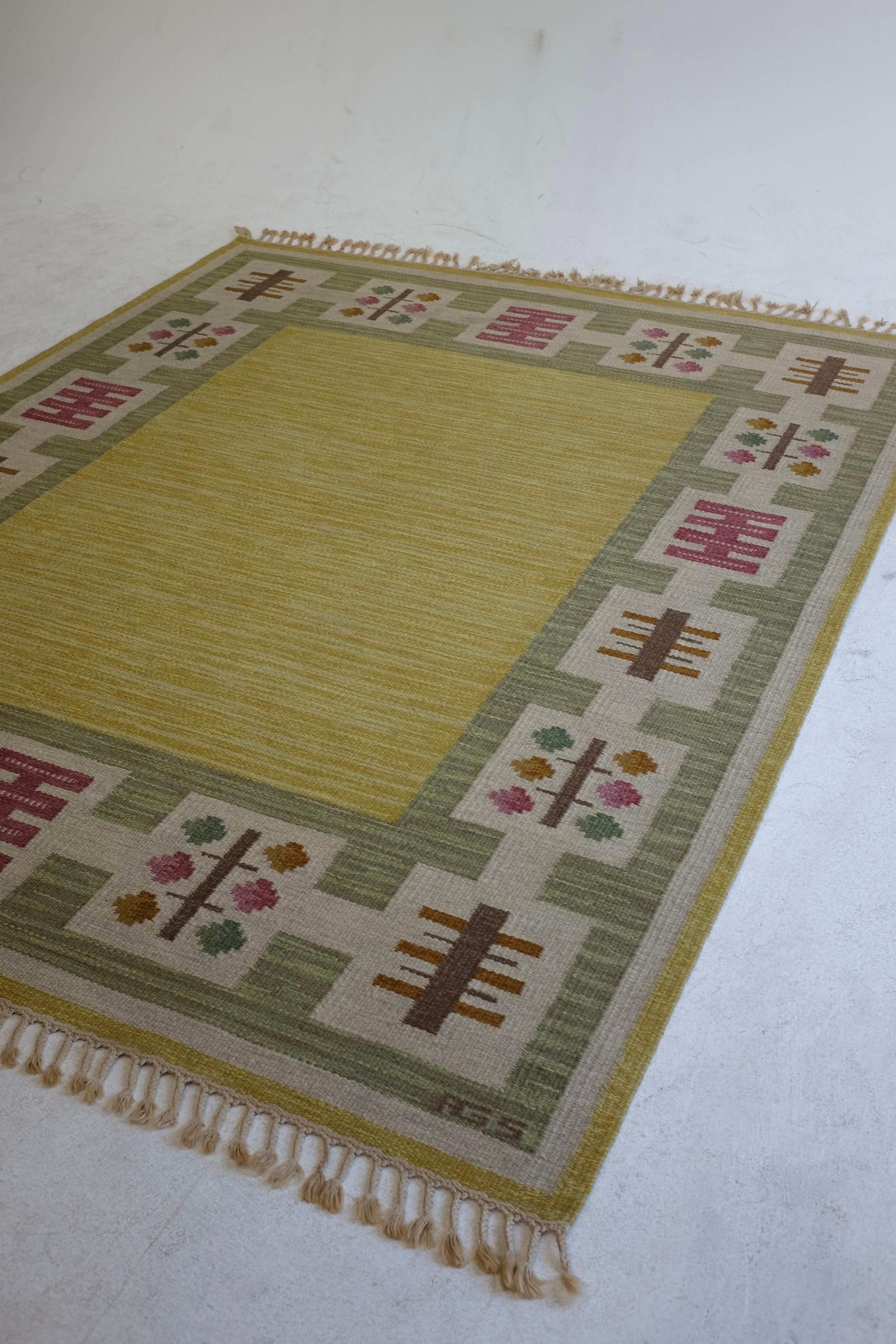 Vintage Swedish Kilim rug by Swedish textile designer Anna Greta Sjöqvist. Beautiful yellow base with a geometric pattern on the edges in green, pink and brown. Designer initials on the lower right hand side. Age appropriate wear with fringes