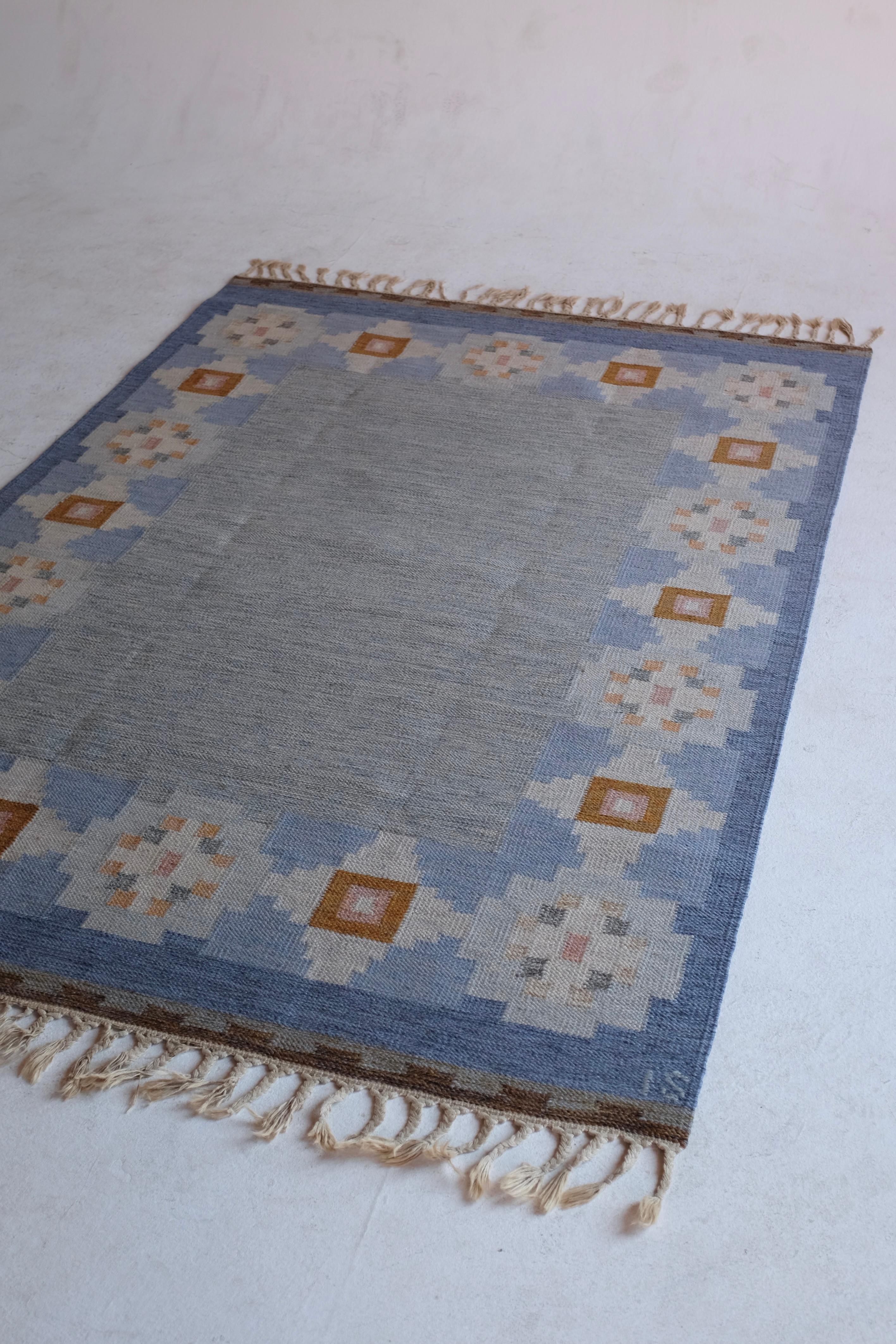 Vintage Mid-Century rug by Swedish textile designer Ingegerd Silow. A blue foundation sits against a geometric flower design along the borders in brown, white and pink shades. In a good condition with some wear to the fringes and small marks on the