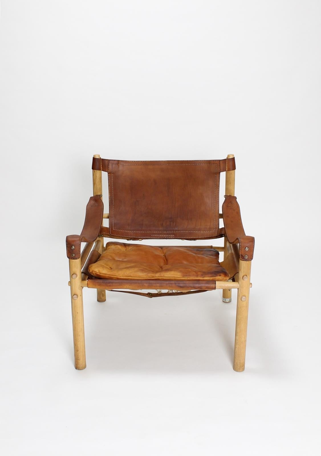 The vintage Swedish midcentury Sirocco Safari chair designed by Arne Norell and produced by Aneby in Sweden in the 1970s. Saddle leather with brass buckles in an ash frame. A patina on the leather, a small tear, crack on the pillow.