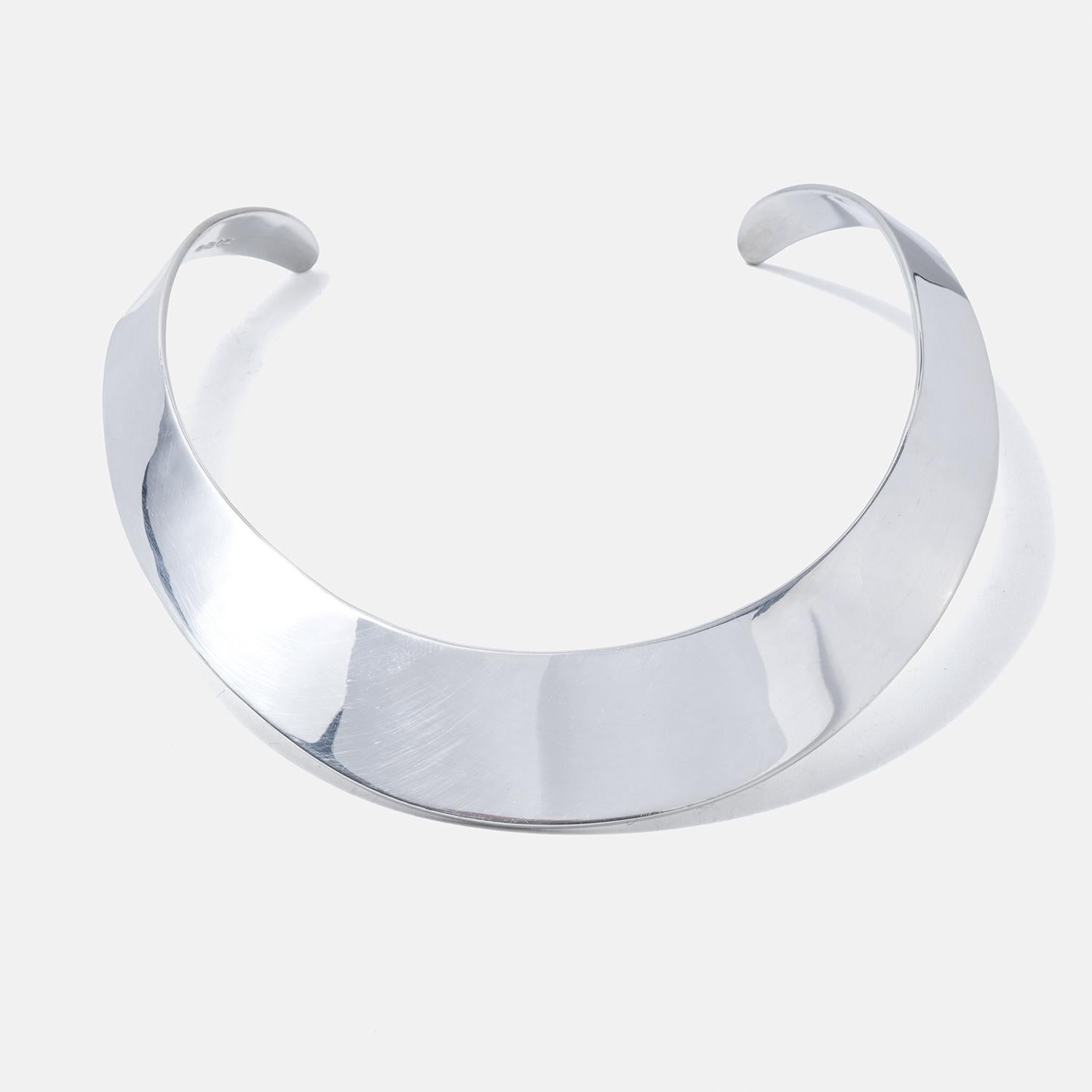Dieser Halsring ist sorgfältig aus Sterlingsilber gefertigt und verfügt über ein breites, festes Band, das sich elegant und bequem um den Hals schmiegt. Die Oberfläche des Silbers glänzt und unterstreicht den Gesamteindruck hochwertiger