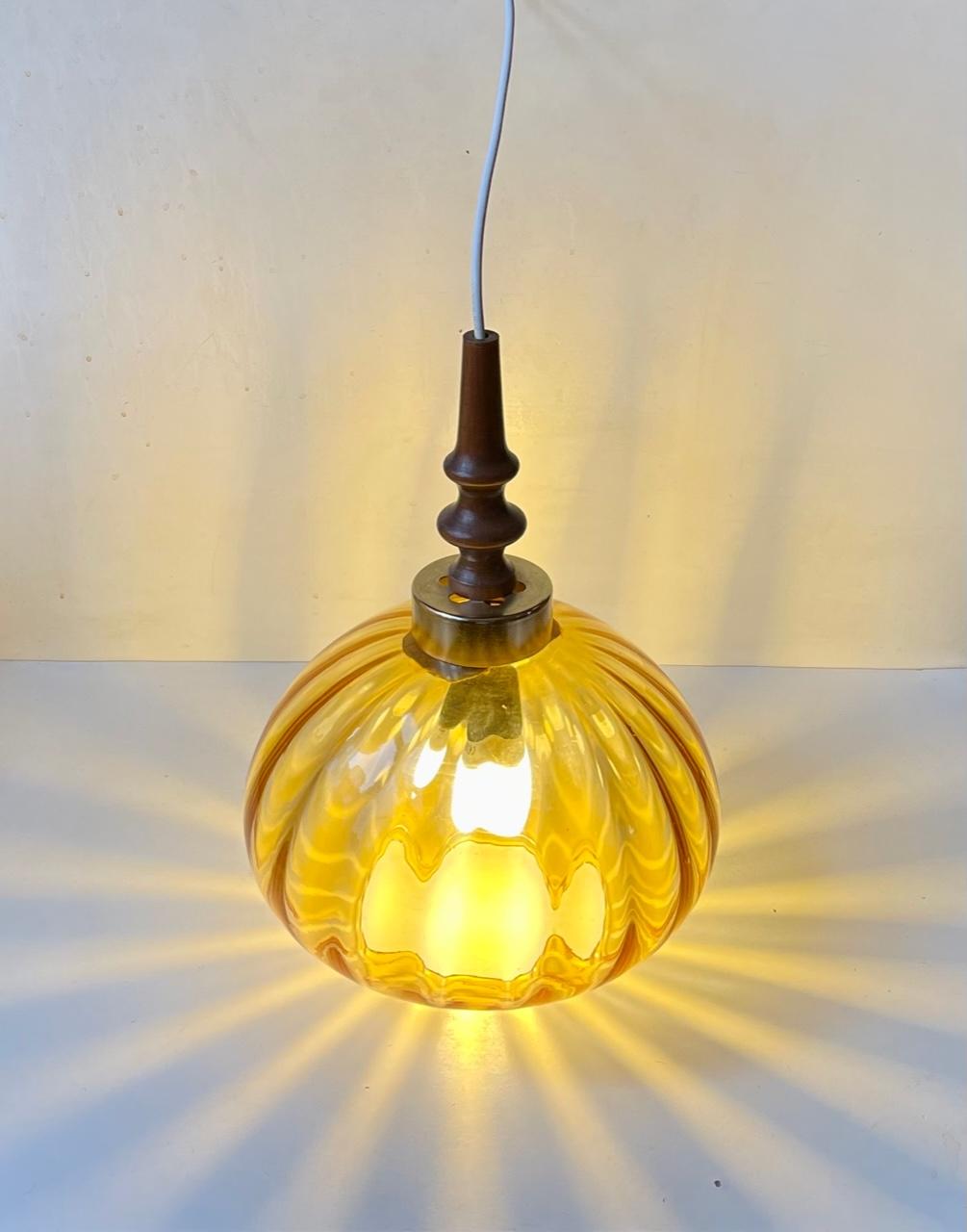 Onion shaped hand-blown hanging light in honey colored optically striped glass. It features a sculptural top in lacquered cherry and perforated brass. Unknown Swedish maker / design in the style of Carl Fagerlund and Orrefors. Measurements: height: